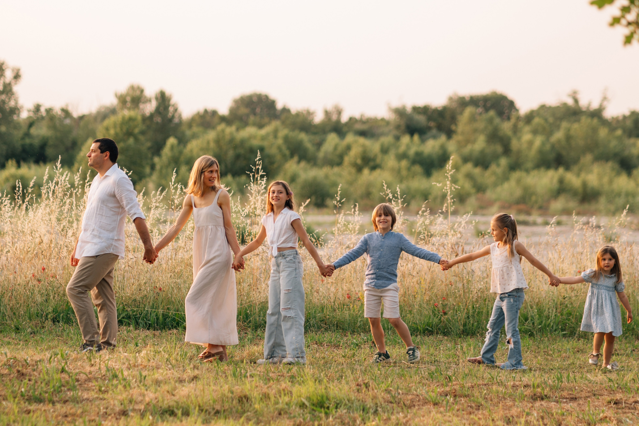Servizio fotografico di famiglia in Italia: genitori e bambini che camminano mano nella mano in un campo al tramonto