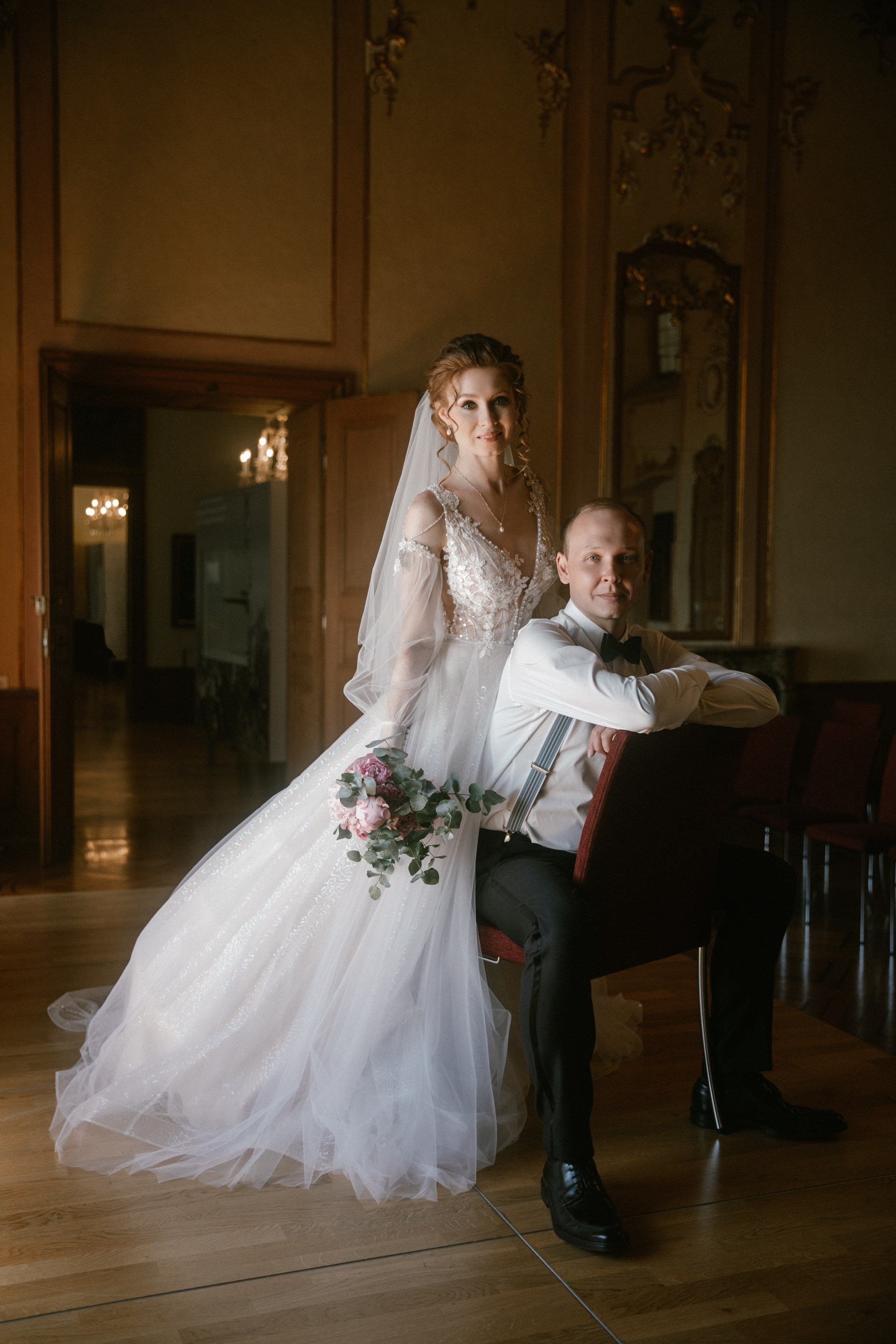 Braut steht mit Blumenstrauß hinter sitzendem Bräutigam – Hochzeit am Bodensee im Schloss Meersburg