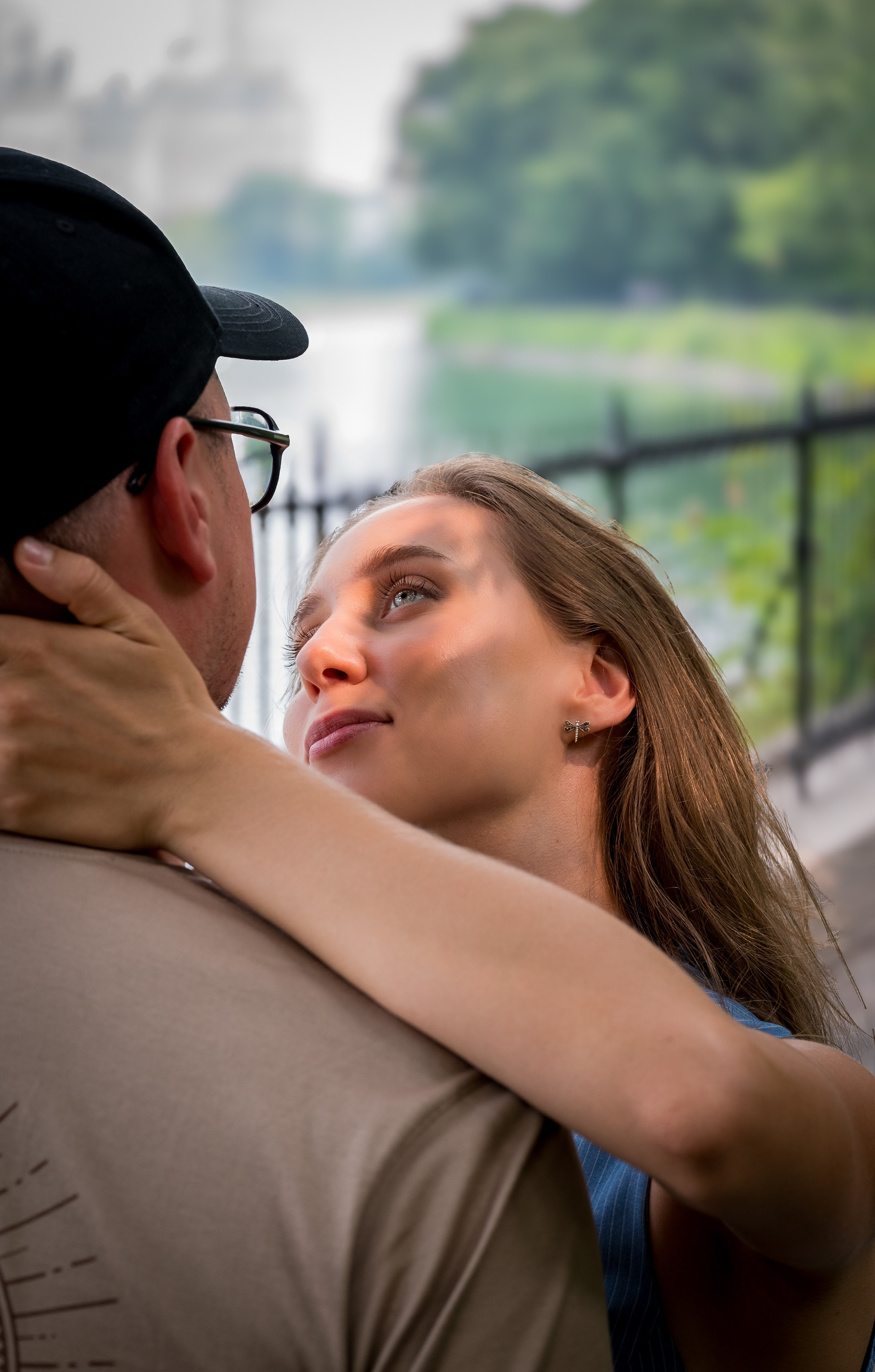 Close-up couple embrace and kiss near a park fence, dreamy background blur, romantic NYC couple portrait.
