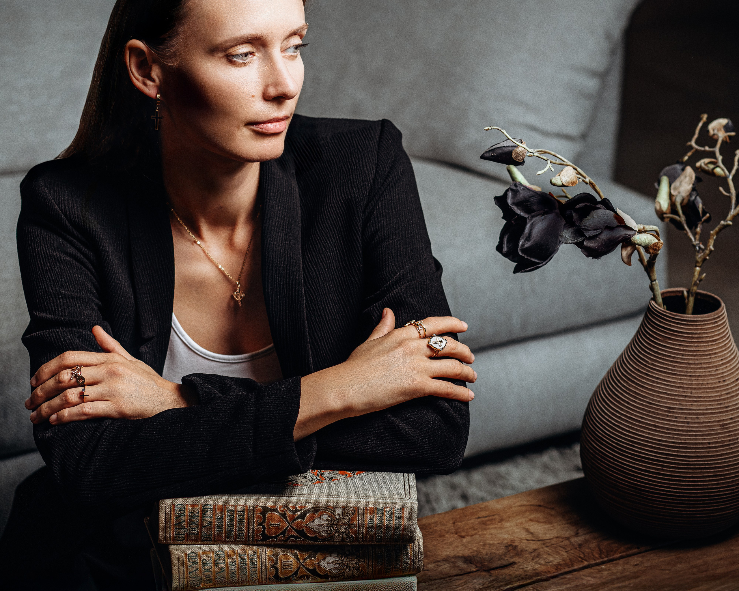 Stylish brand portrait captured in Valencia, Spain, featuring a woman in a black blazer adorned with elegant rings and a cross earring, posed beside vintage books — ideal for content and product photoshoots in Valencia tailored for lifestyle brands, jewelry labels, and personal branding.
