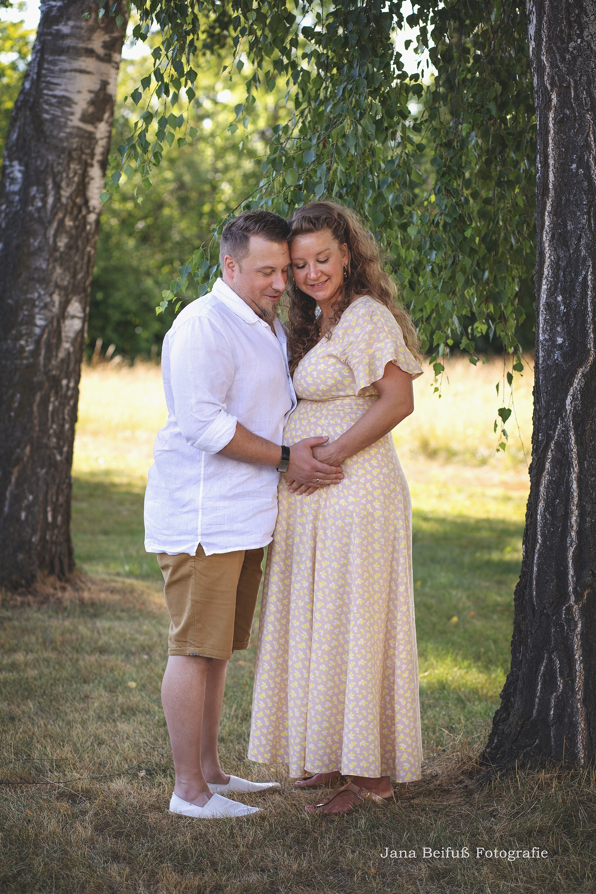werdende Eltern schauen auf den Babybauch stehen auf der Wiese in Weißenhorn - Schwangerschaftsfotograf Jana Beifuß in Weißenhorn bei Ulm