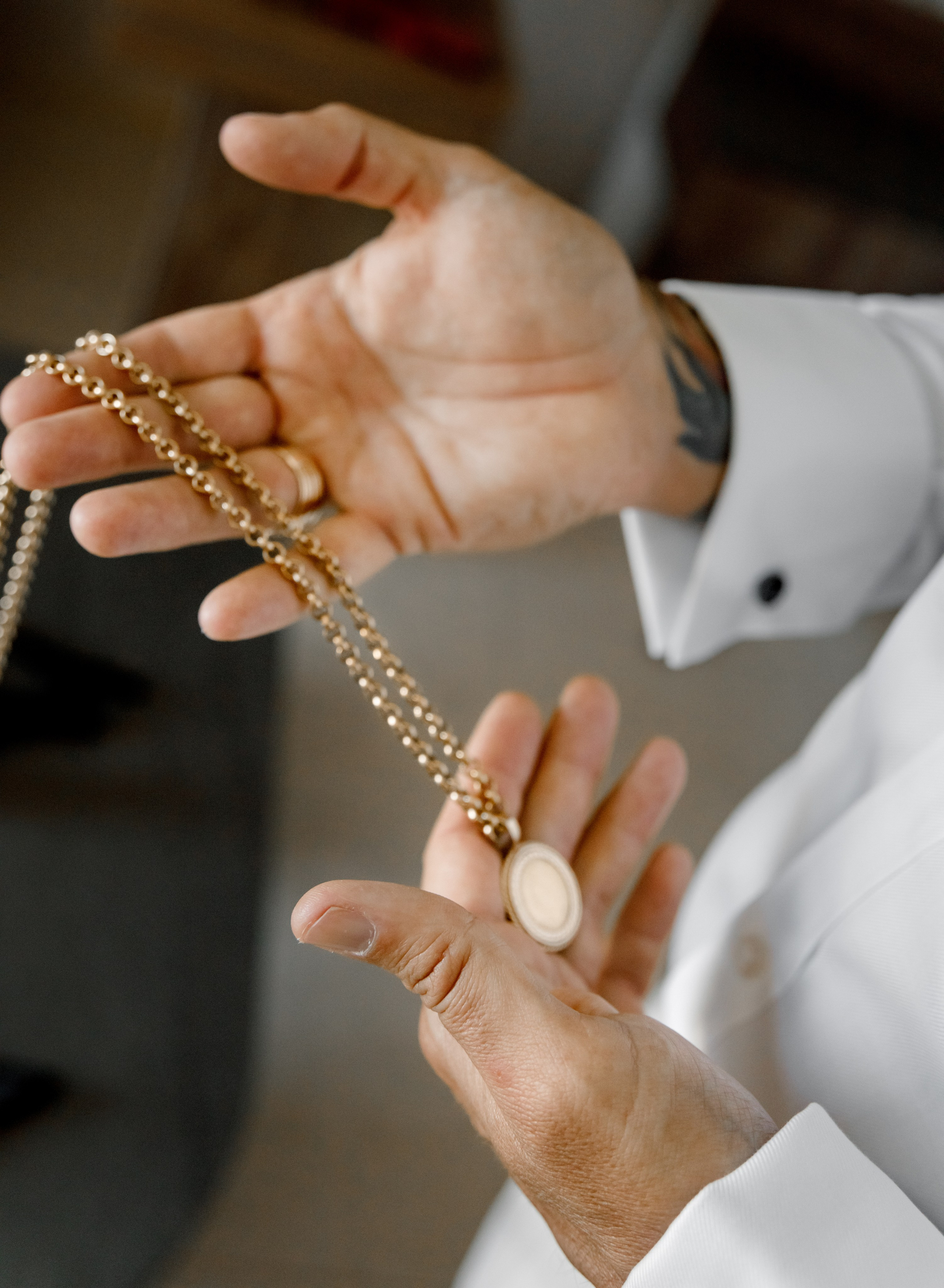 Close-up of the groom's hands holding a thick gold chain, his fingers gently tracing its links.