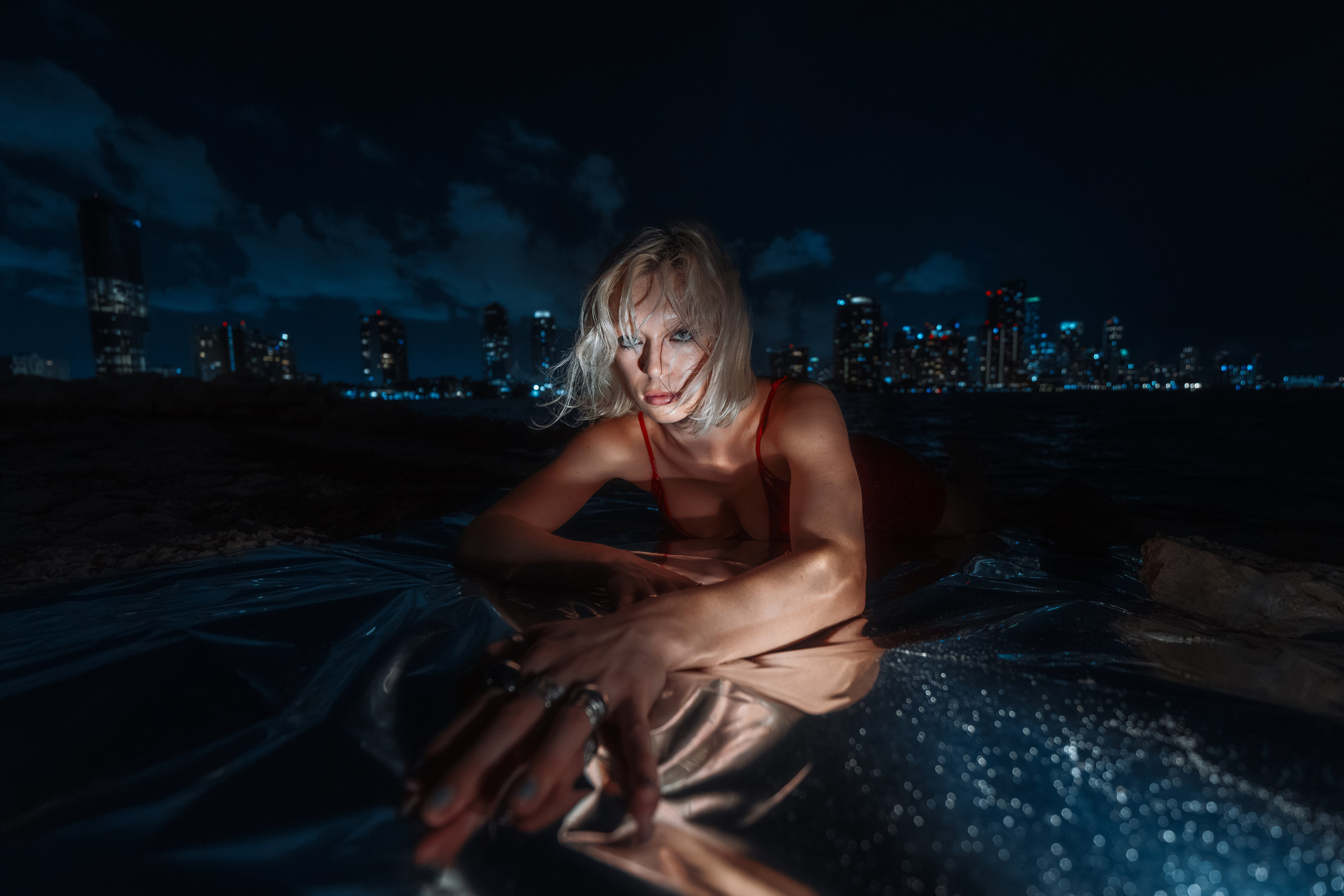 Low-angle portrait with city lights defining the horizon line. The subject appears bold and expansive. Mylar reflections