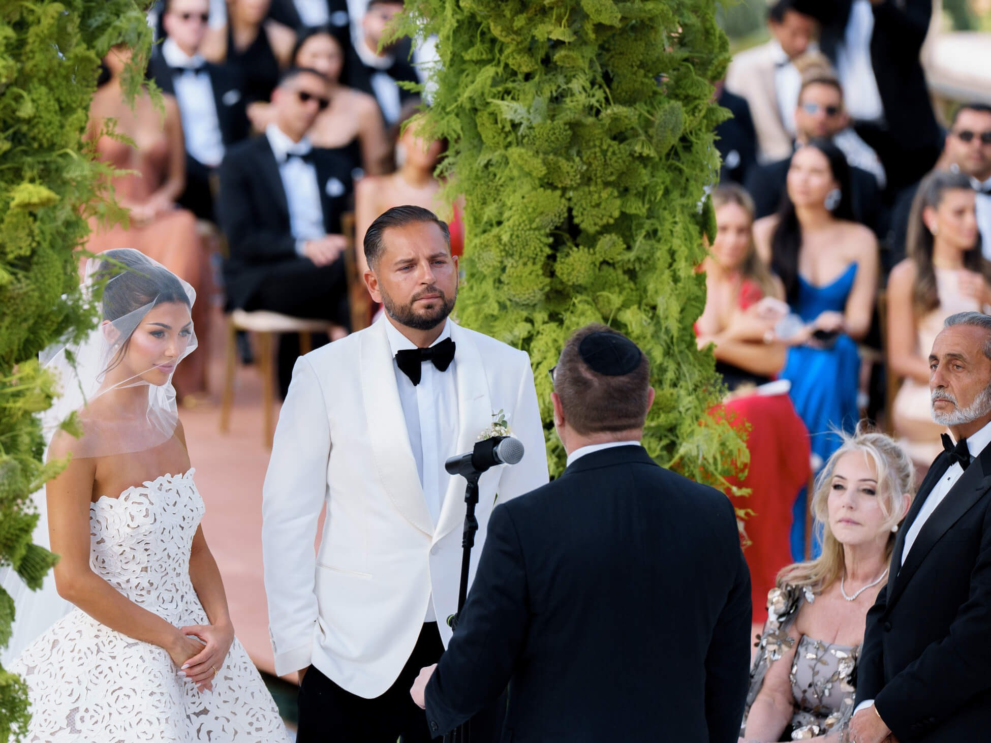Bride and groom facing each other at the altar beneath a greenery arch, veil catching the light, surrounded by guests at a destination wedding in Morocco