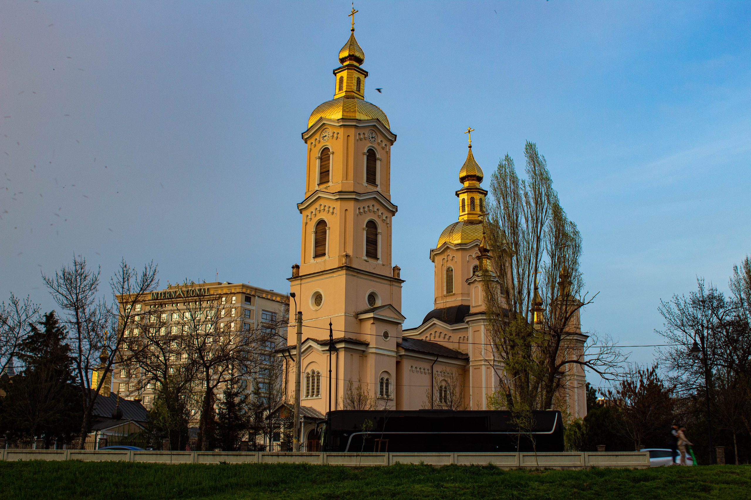 Historic church tower glowing in warm evening light with trees in the foreground.