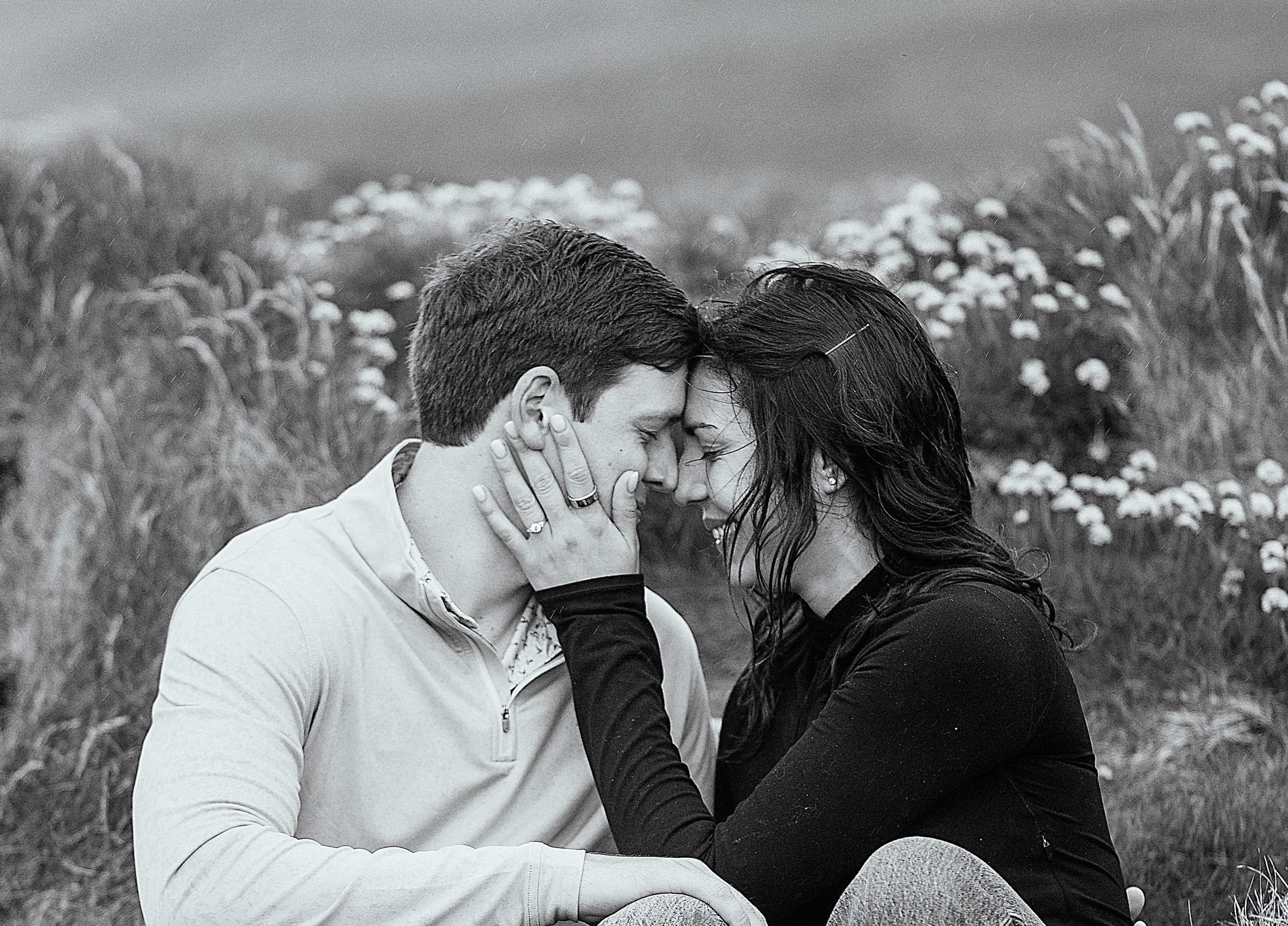 Black and white photograph of an engaged couple sitting together in a field of flowers near Doolin, Ireland.