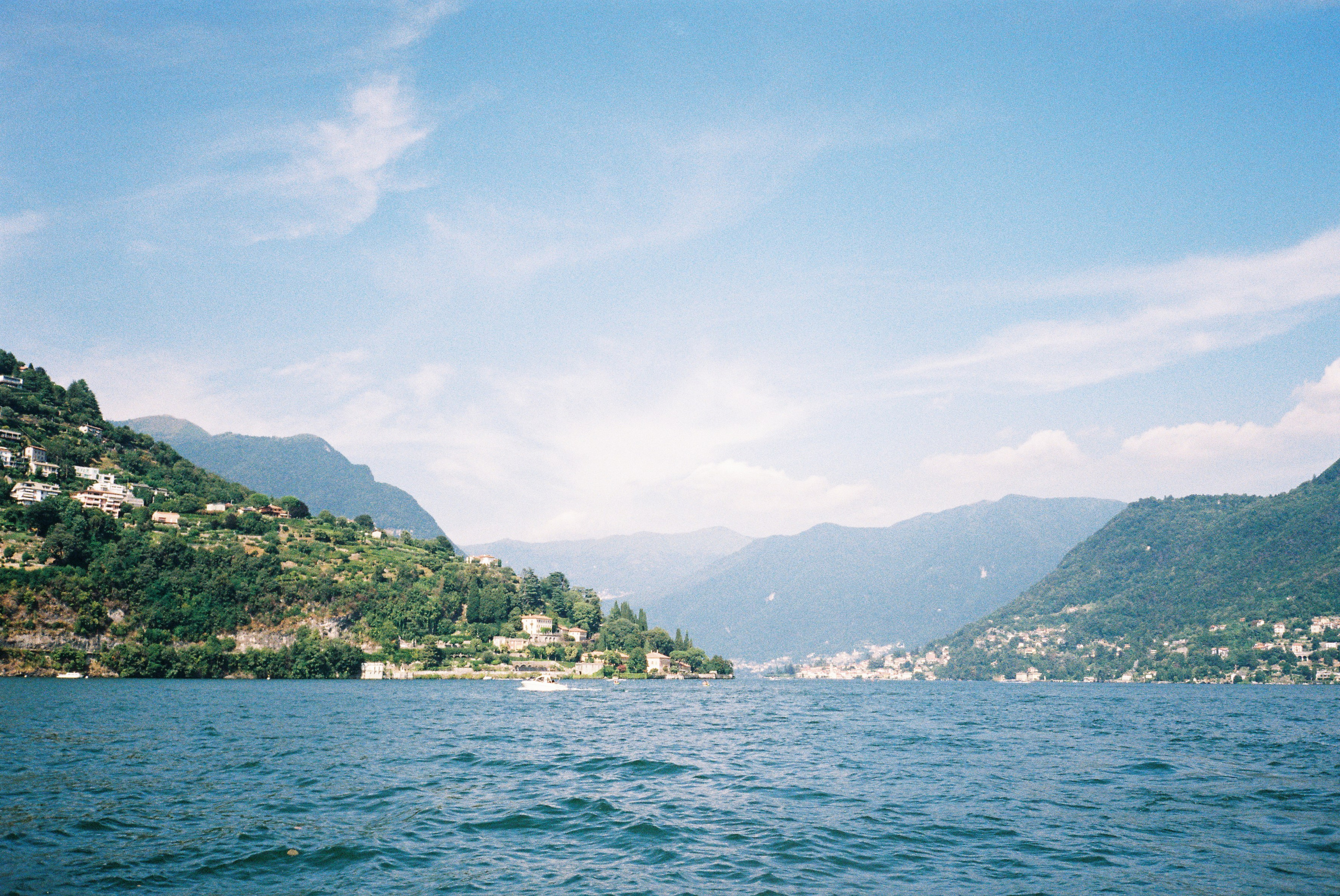 Scenic lake view framed by green hills under a clear blue sky, evoking serene tranquility.