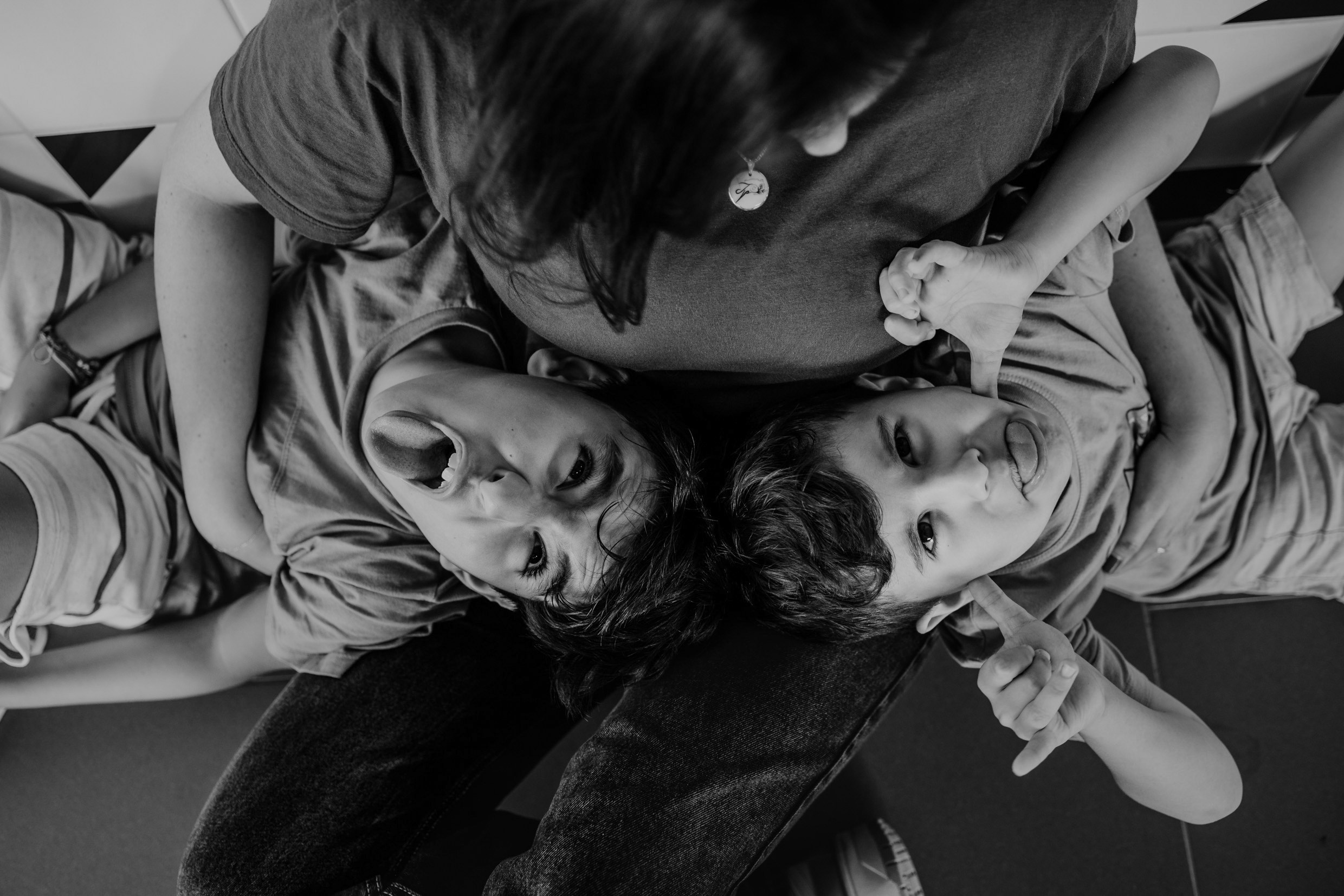 Irmãos fazendo careta deitados no colo da mãe