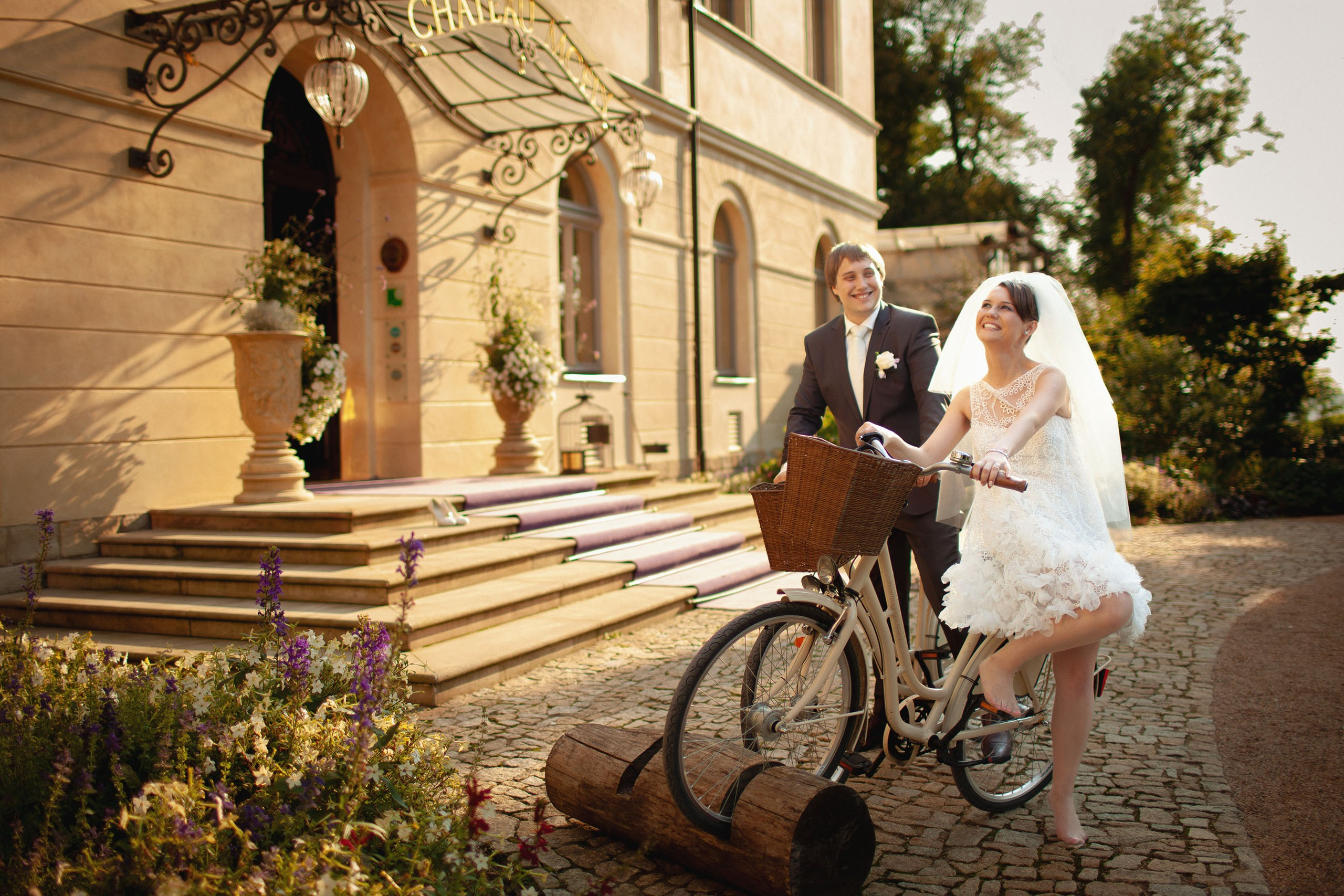 Happy newlyweds share a moment of laughter besides bikes near the front entry of the historic Chateau Mcely.
