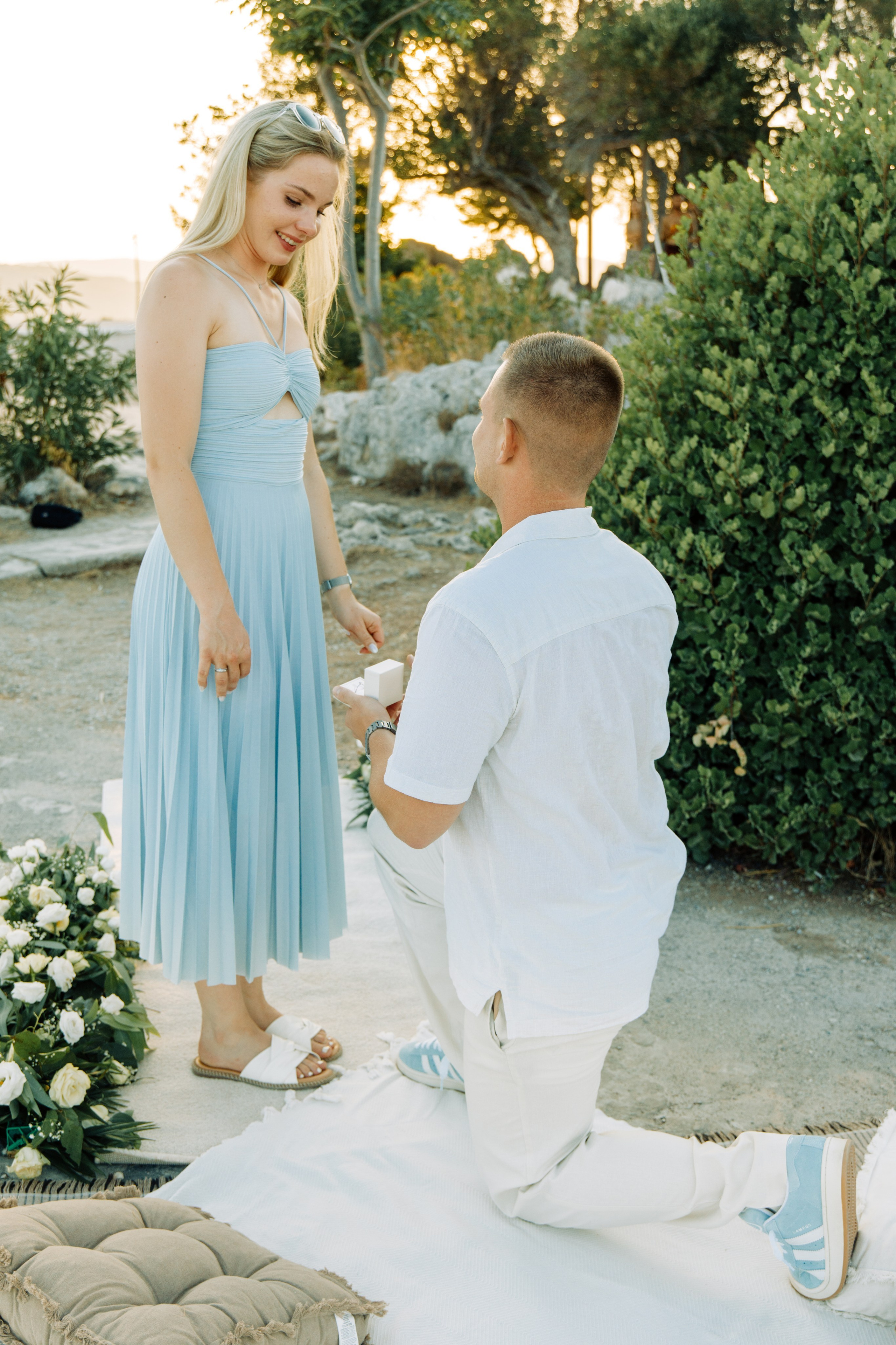 Marriage proposal in Rhodes 💍 man kneels in front of woman with ring during a romantic outdoor proposal with flowers and sunset in Greece.