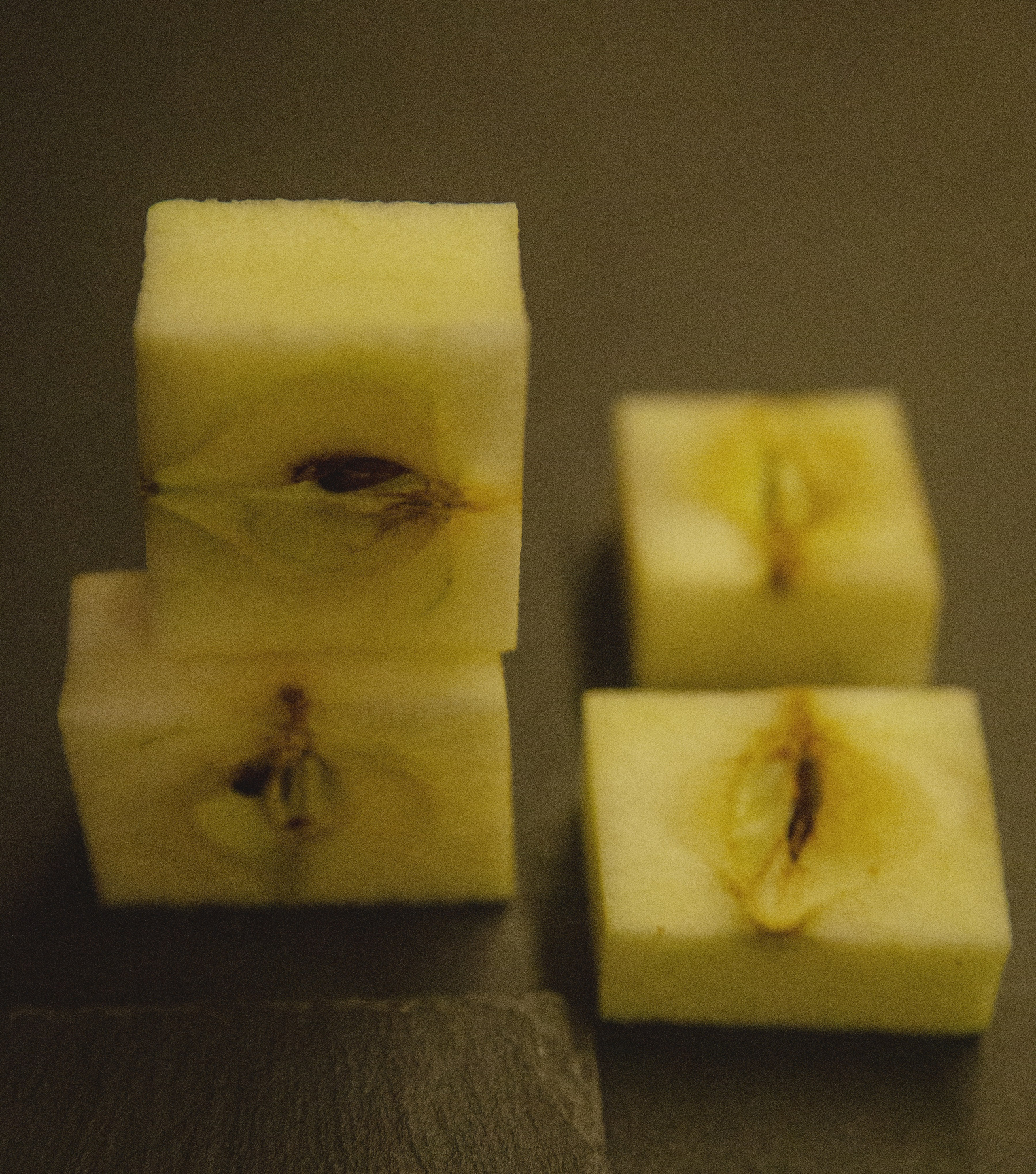 Close-up photo of precisely cut apple cubes stacked vertically, highlighting the exposed seeds and minimalist aesthetic in soft lighting