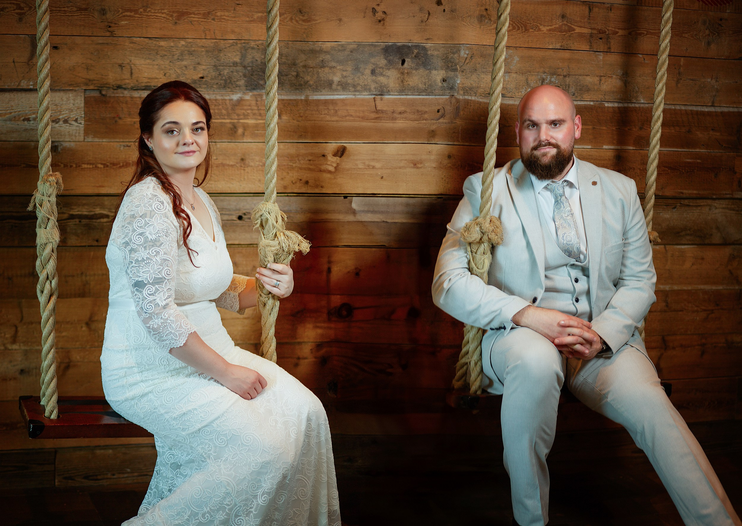 Creative wedding portrait of a bride and groom sitting on decorative wooden indoor swings. Unique wedding photography services in Dublin.