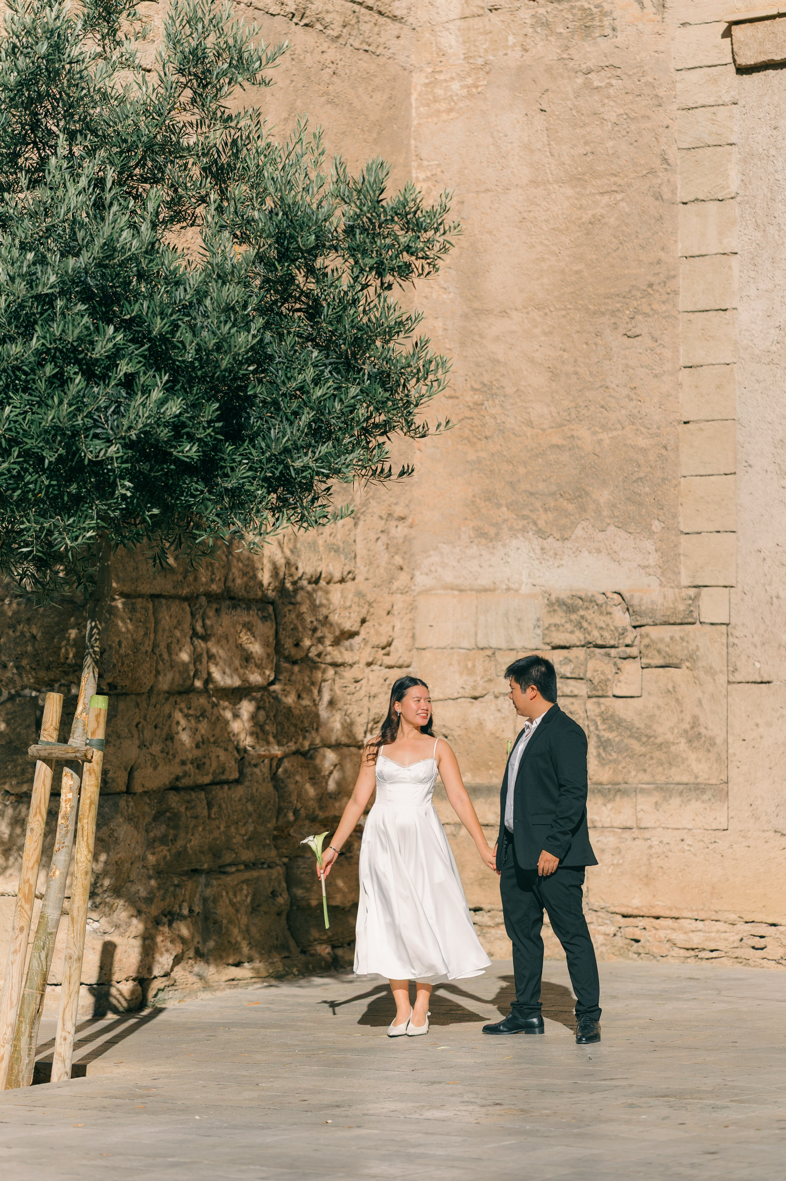 Wedding couple holding hands beside the historic stone walls of Palma