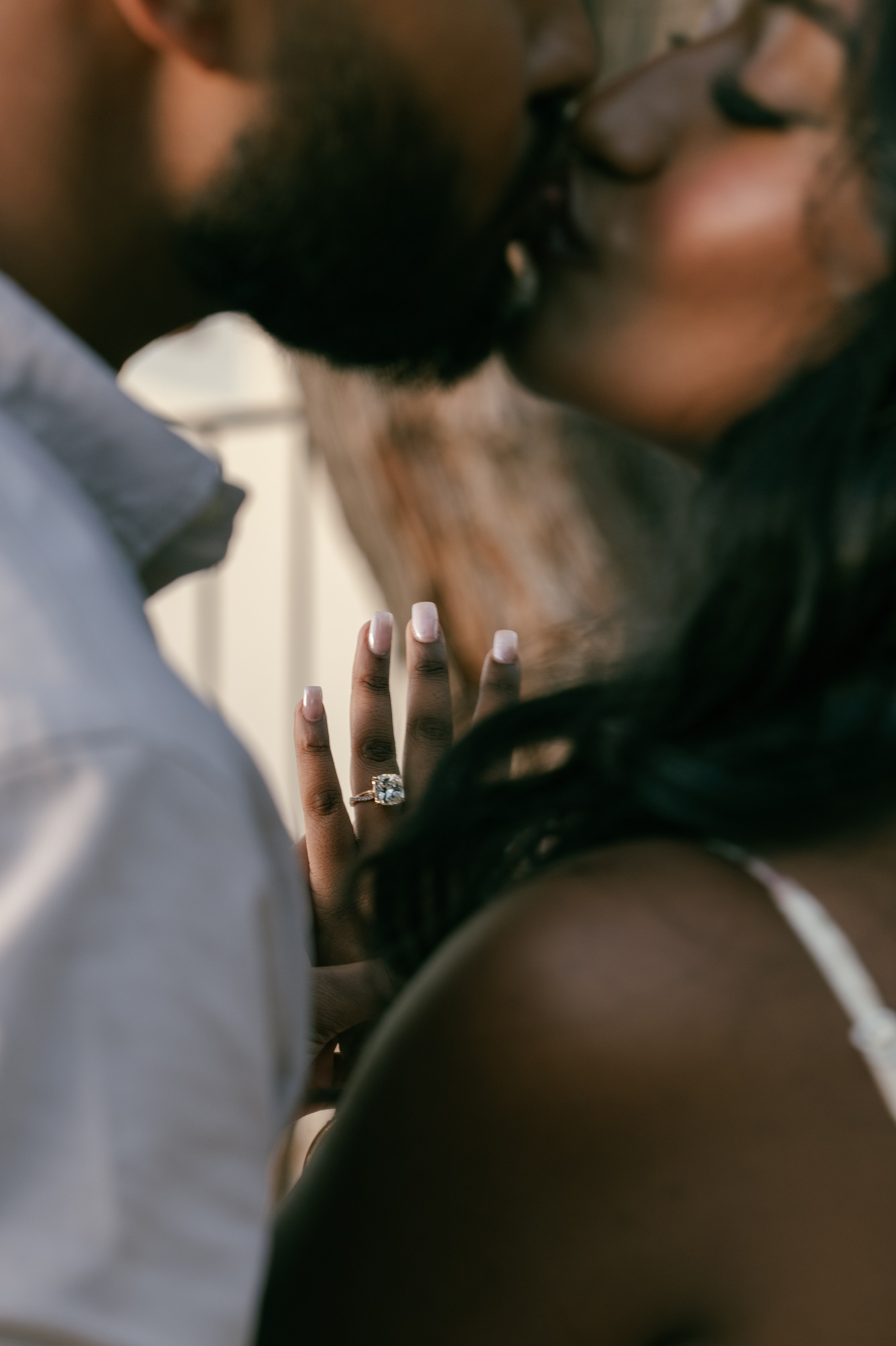 Close-up of a newly engaged couple kissing, with her engagement ring visible.