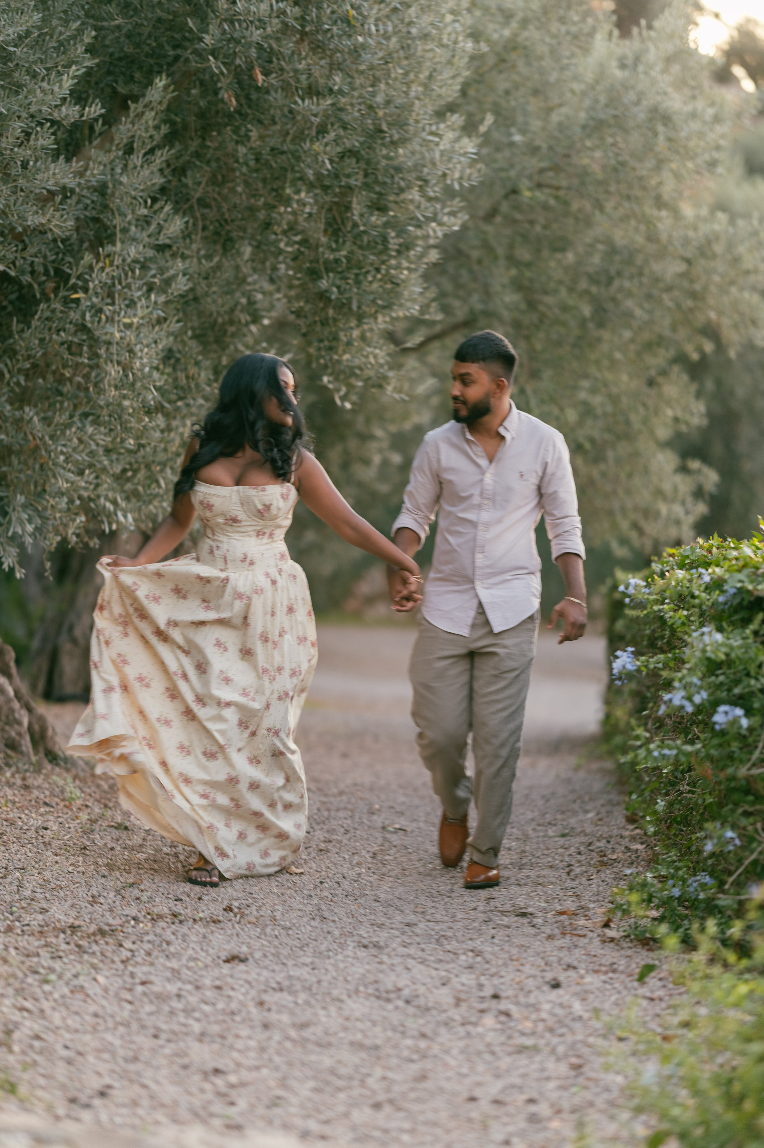 A newly engaged couple walking hand in hand among olive trees in Sóller, Mallorca.