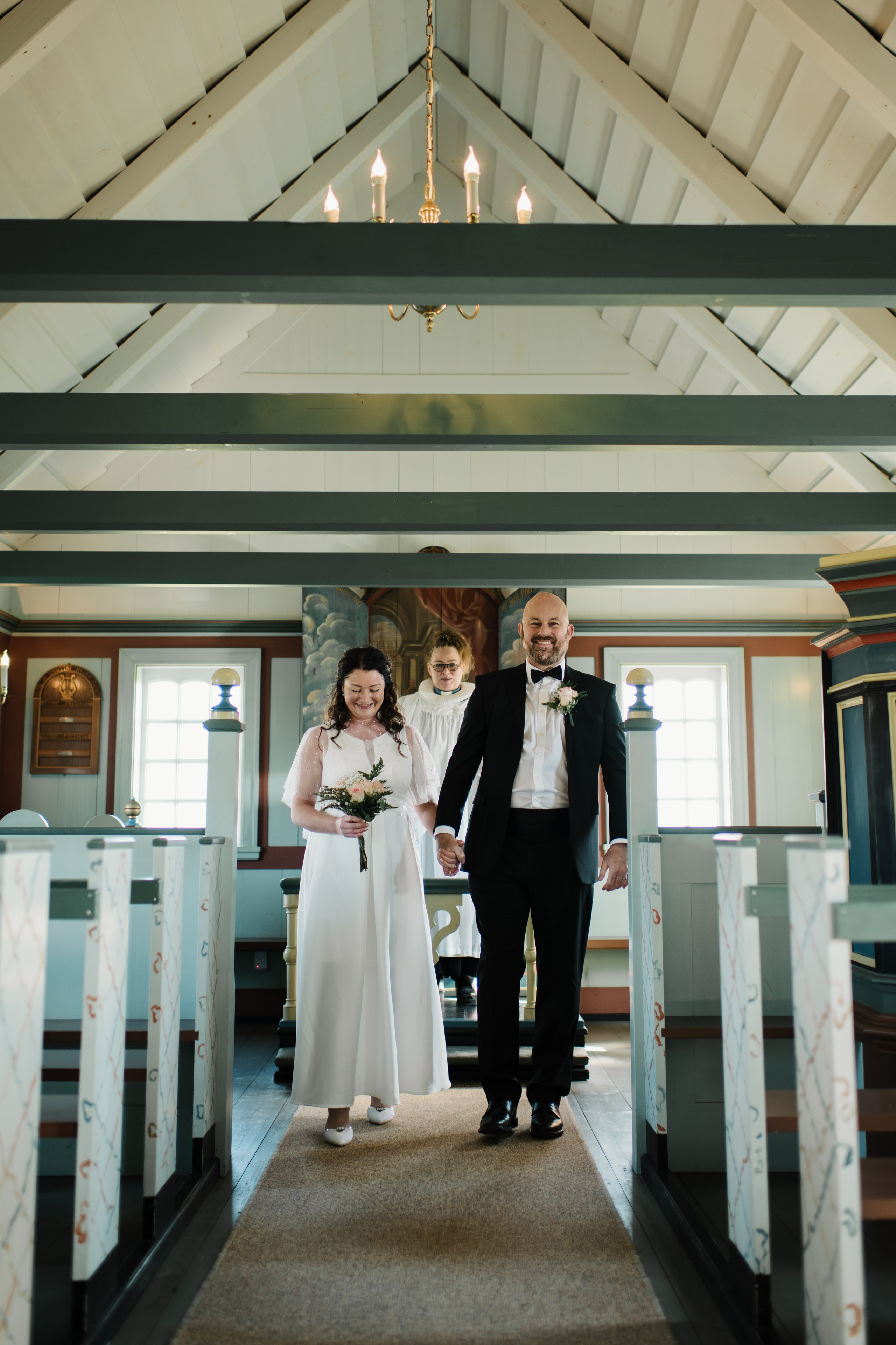 Intimate embrace between the bride and groom near the black church of Búðir, framed by rolling hills and an overcast sky.
