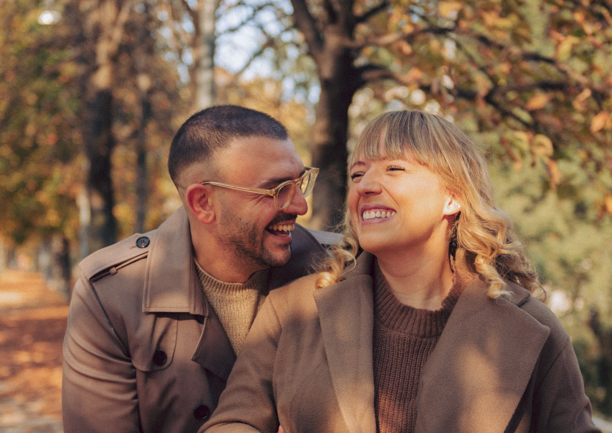 Playful and romantic autumn couple photos captured in warm golden light. The couple shares genuine laughter and natural moments while walking through a park filled with fall colors. Perfect inspiration for candid couple poses, lifestyle autumn photography, and cozy fall couple sessions. Ideal for those who love warm tones, spontaneity, and authentic emotions. autumn couple photoshoot, candid couple photography, fall couple session, natural couple poses, lifestyle couple photos, warm tones photography, cozy fall inspiration, playful couple moments, outdoor romantic photoshoot, golden hour fall aesthetic