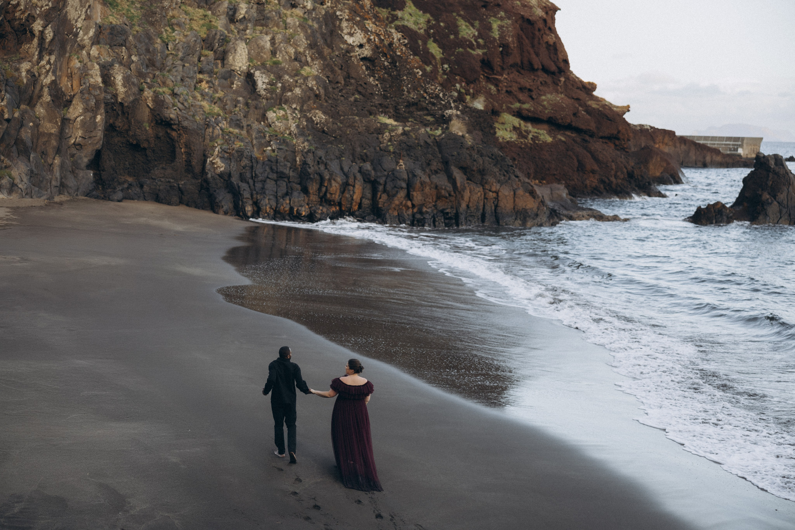 A glowing expectant mother standing on a cliff overlooking the ocean in Madeira, her dress flowing gently in the wind as the golden sunset casts a warm glow.