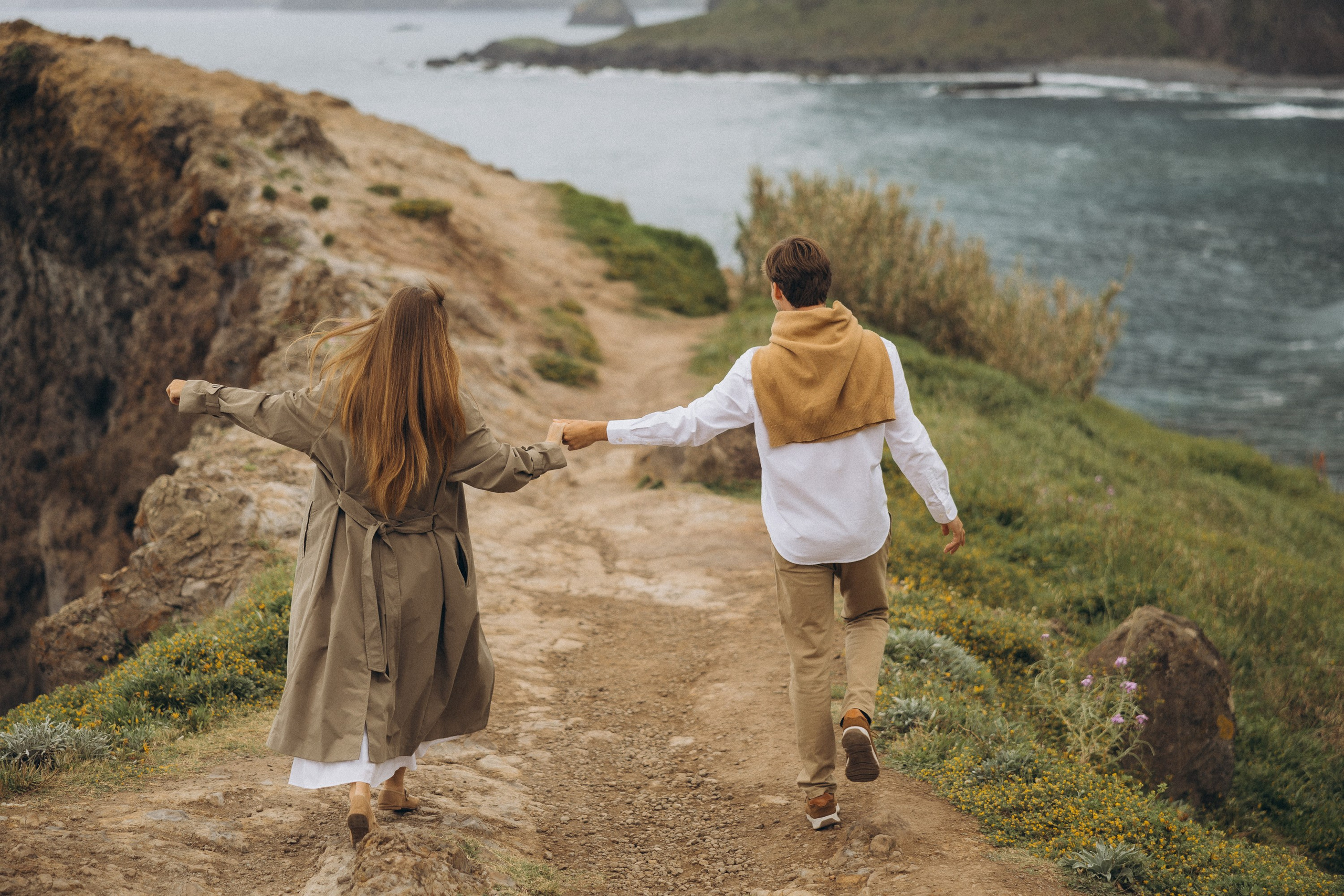 Beautiful engagement moment by the ocean in Madeira, Portugal, as one partner kneels to propose while waves crash in the background