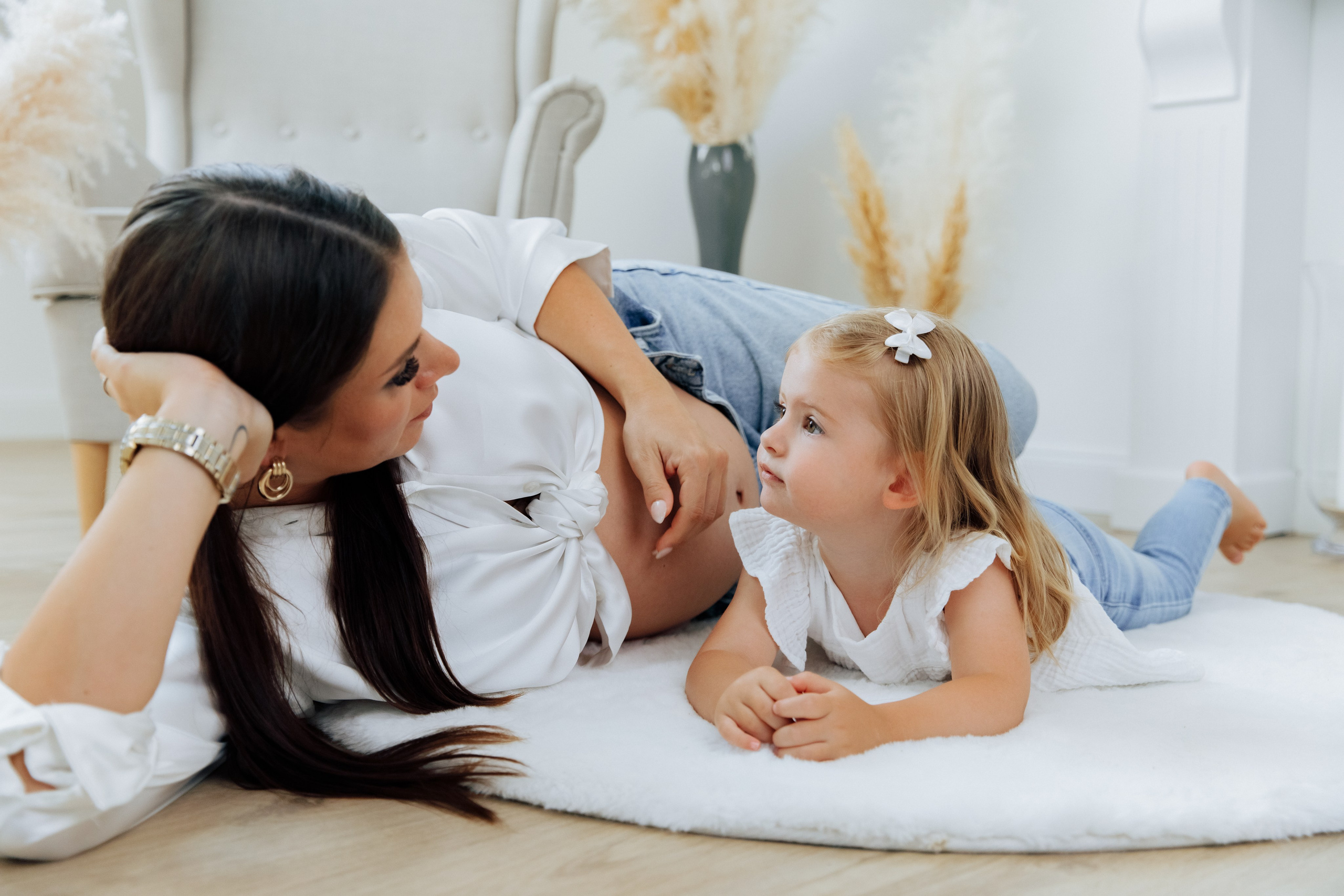 Mutter und Tochter liegen auf dem Teppich im Fotostudio, Babybauch sichtbar.