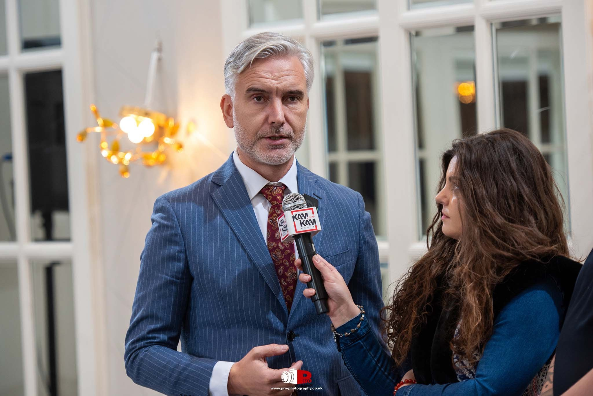 A business executive in a pinstripe suit is being interviewed by a journalist holding a microphone.