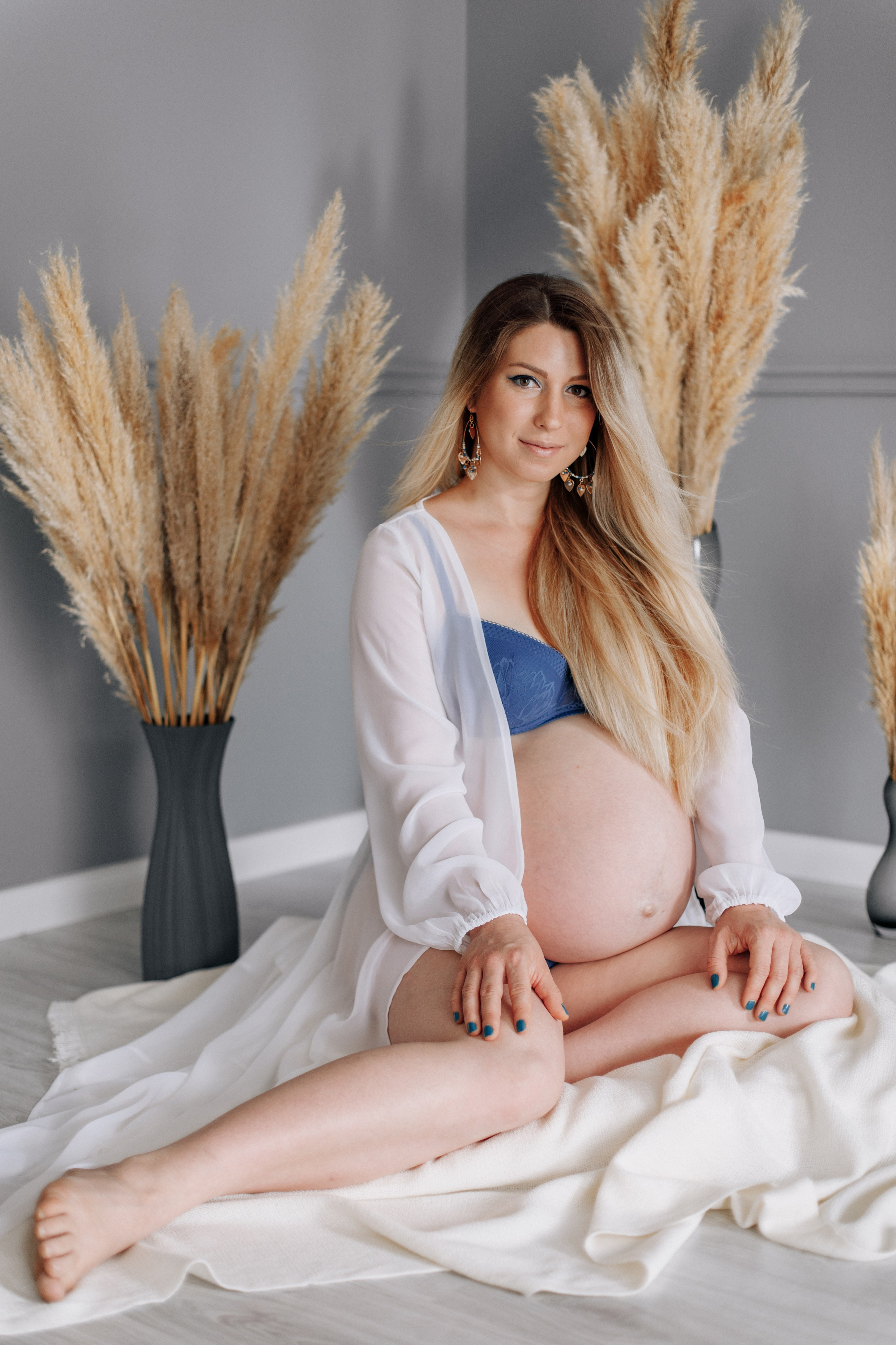 Schwangere Frau in Unterwäsche sitzt im Fotostudio, umgeben von Pampasgras.