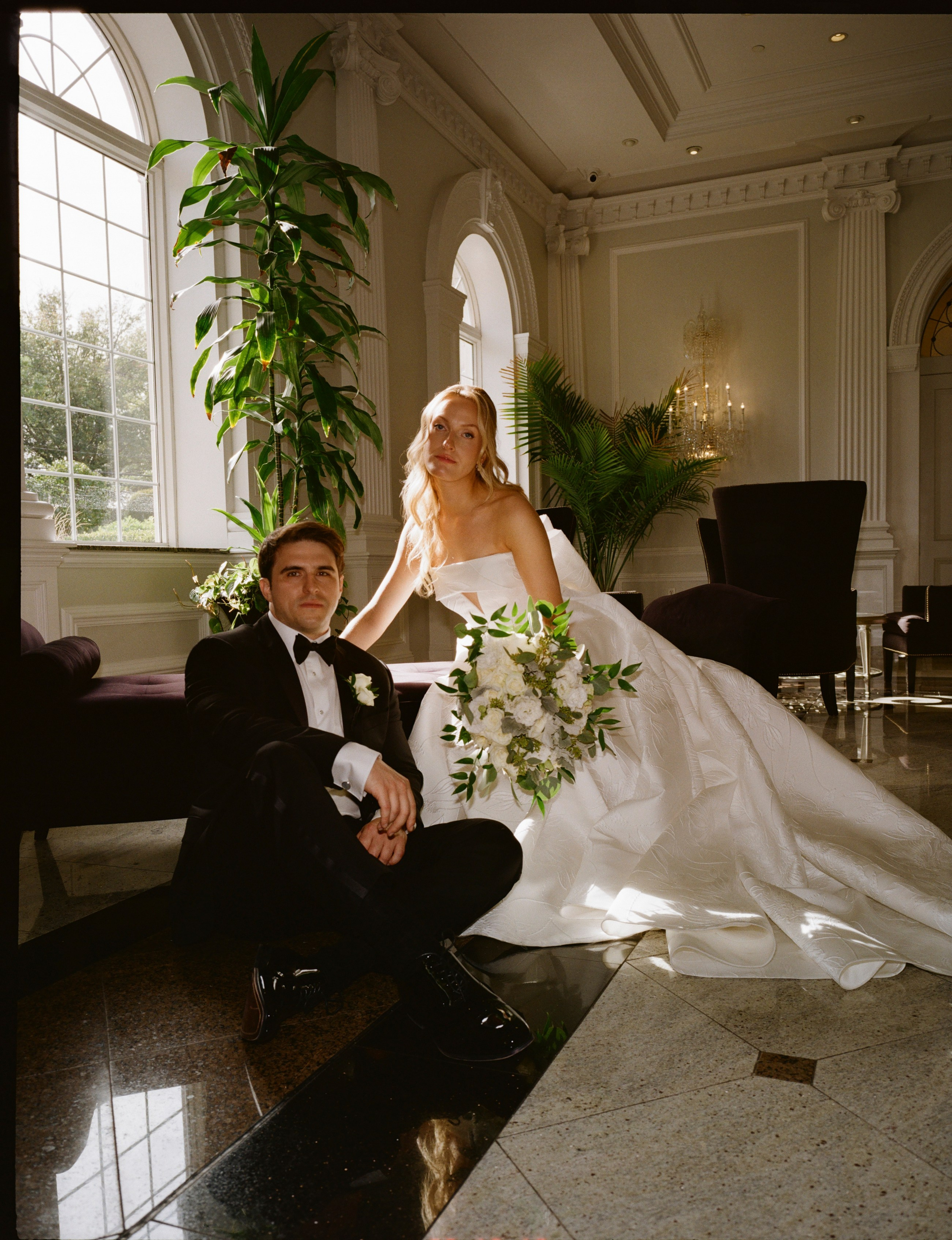 Elegant bridal portrait of Emily reclining indoors with her wedding dress flowing across the sofa