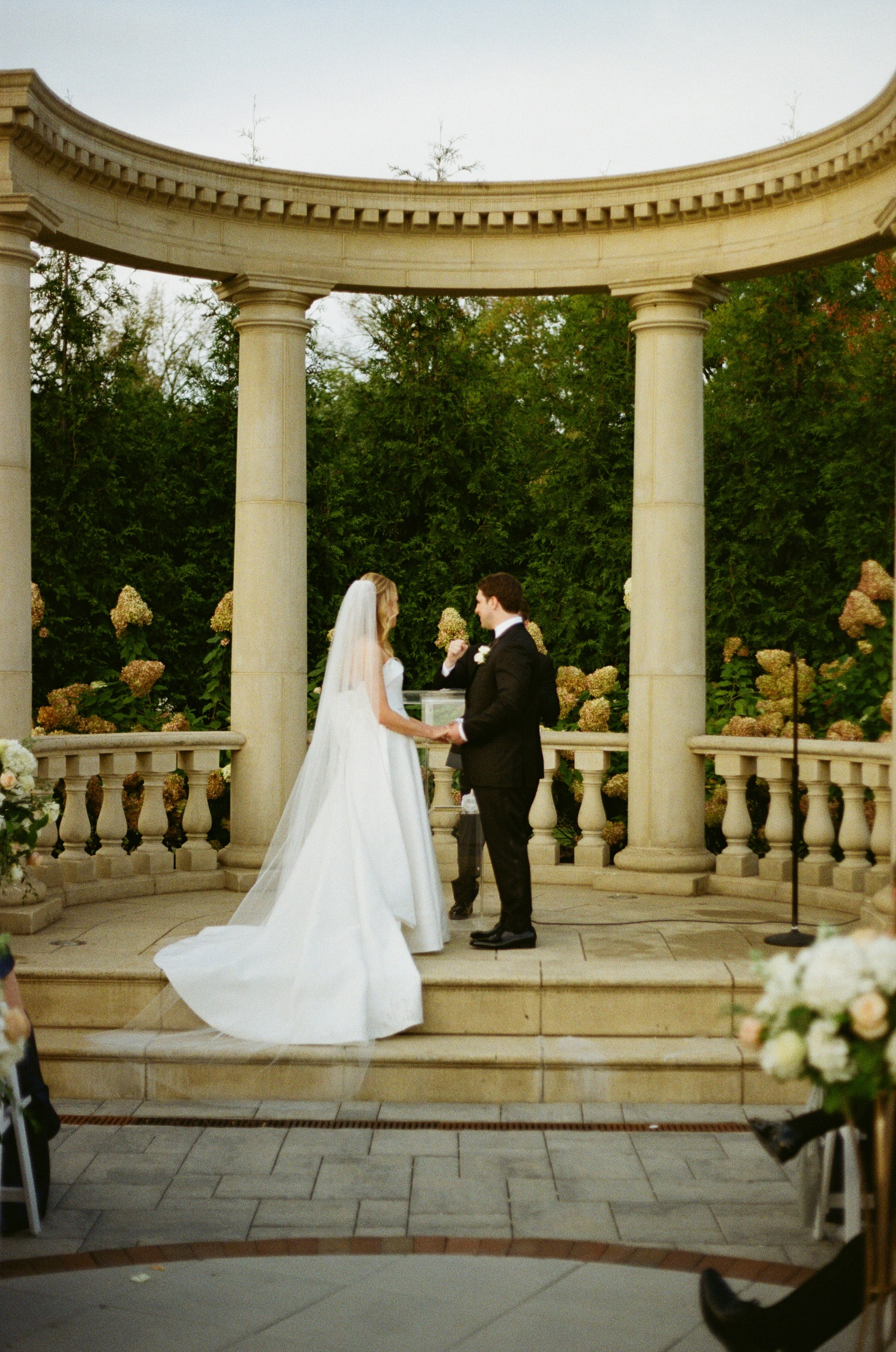 Wide wedding portrait of Emily and Michael beneath the garden pavilion at The Rockleigh