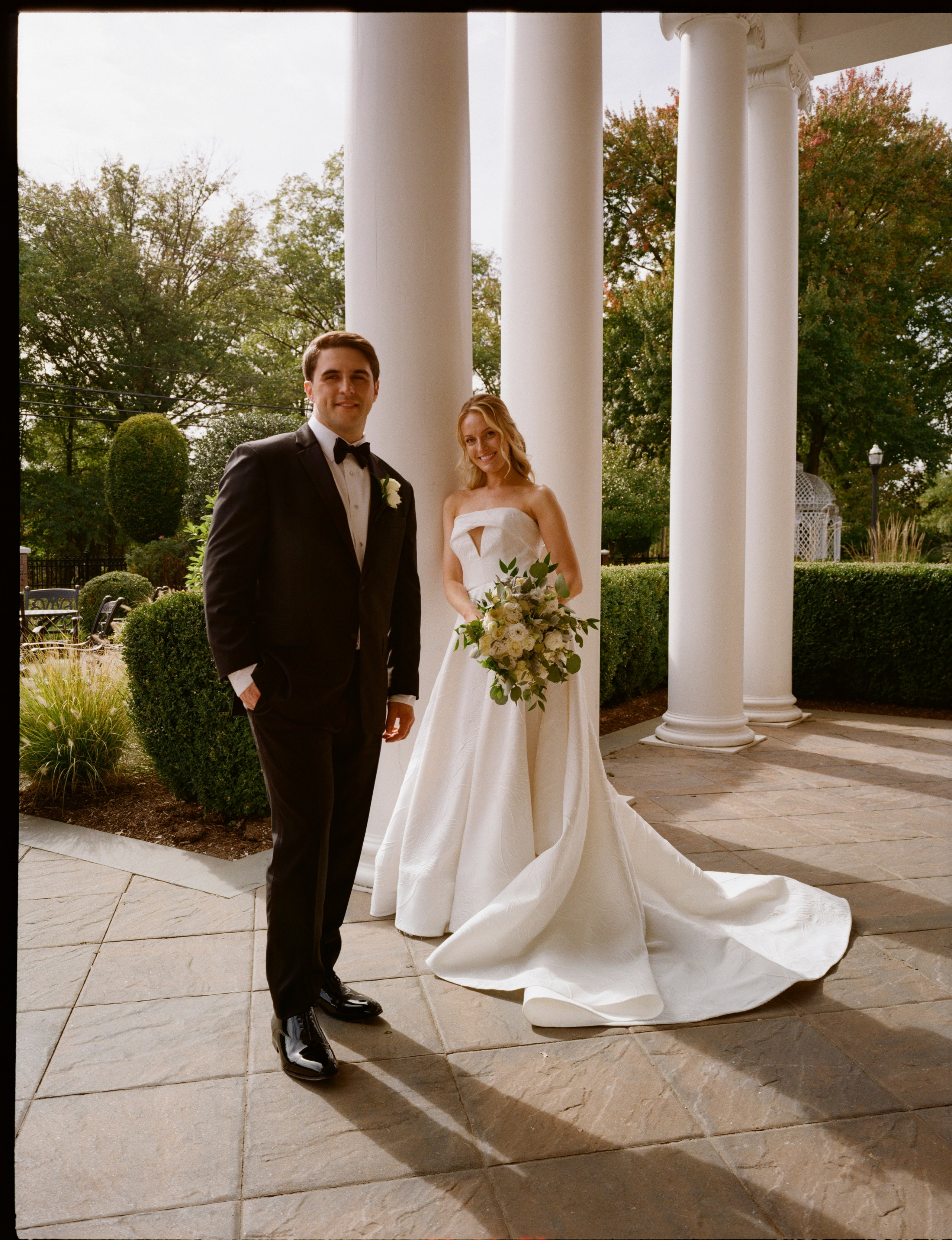 Emily and Michael posing beside the white columns at The Rockleigh wedding venue