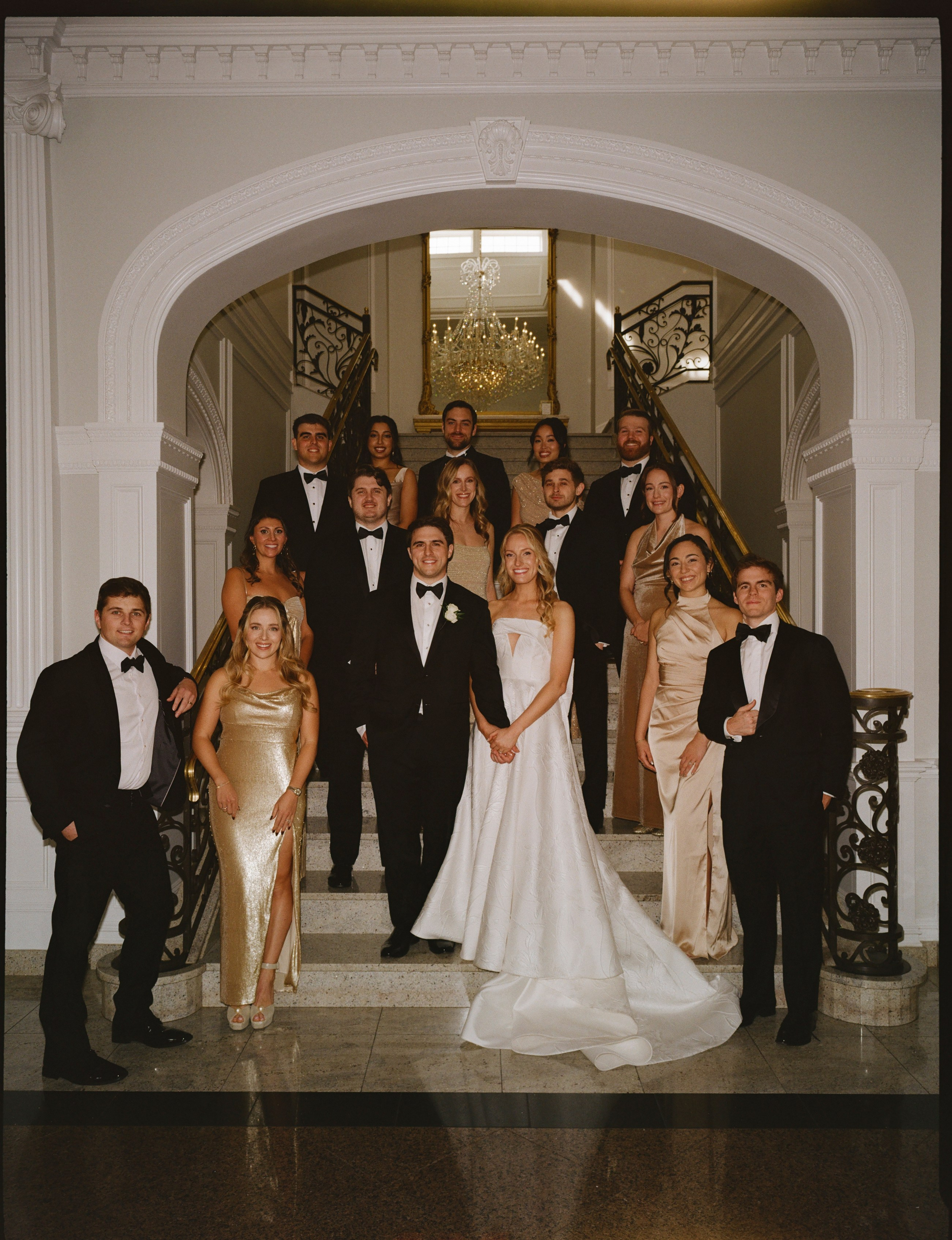 Emily and Michael posing with their wedding party beneath an elegant archway