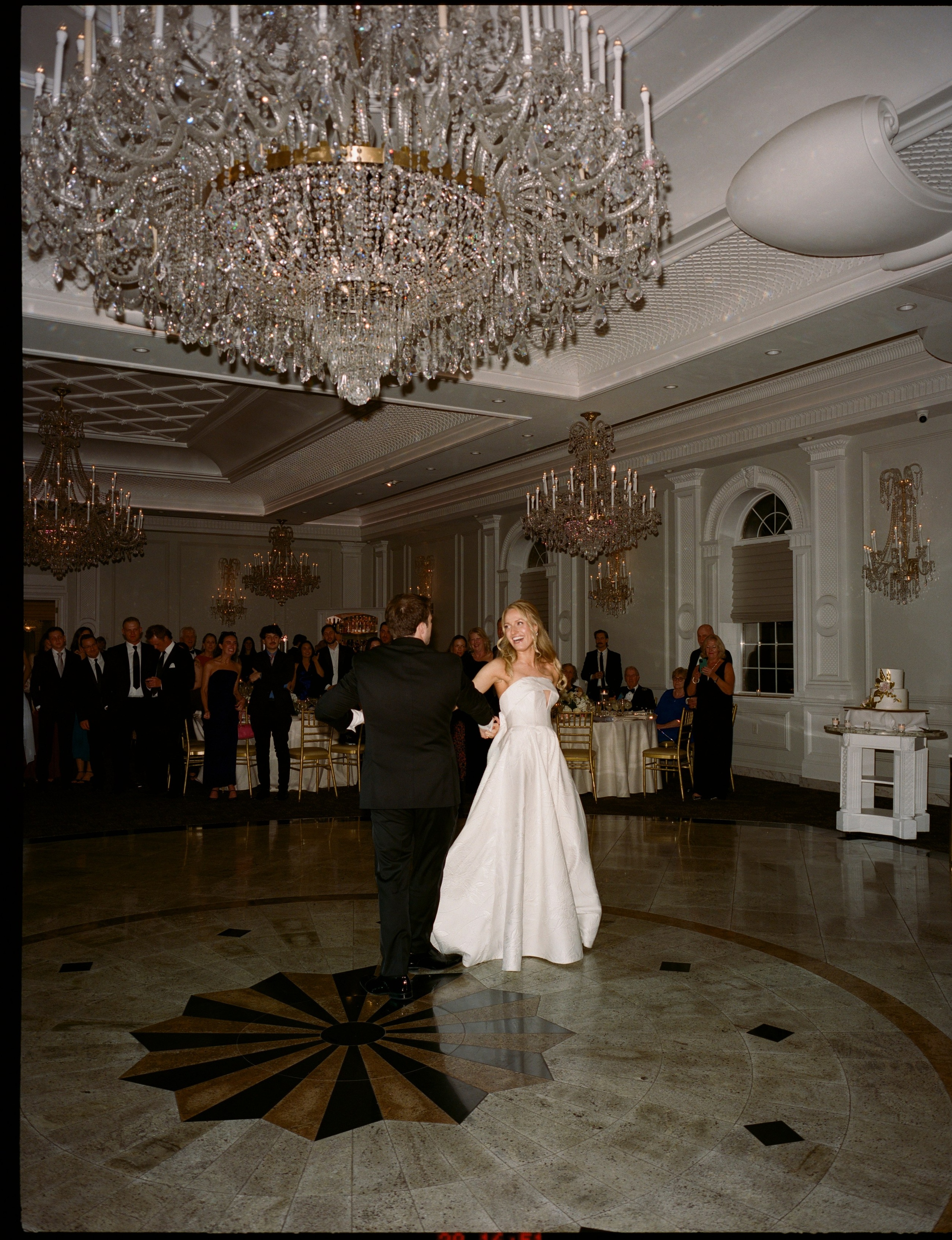 Wide editorial wedding photograph featuring the elegant ballroom and chandeliers