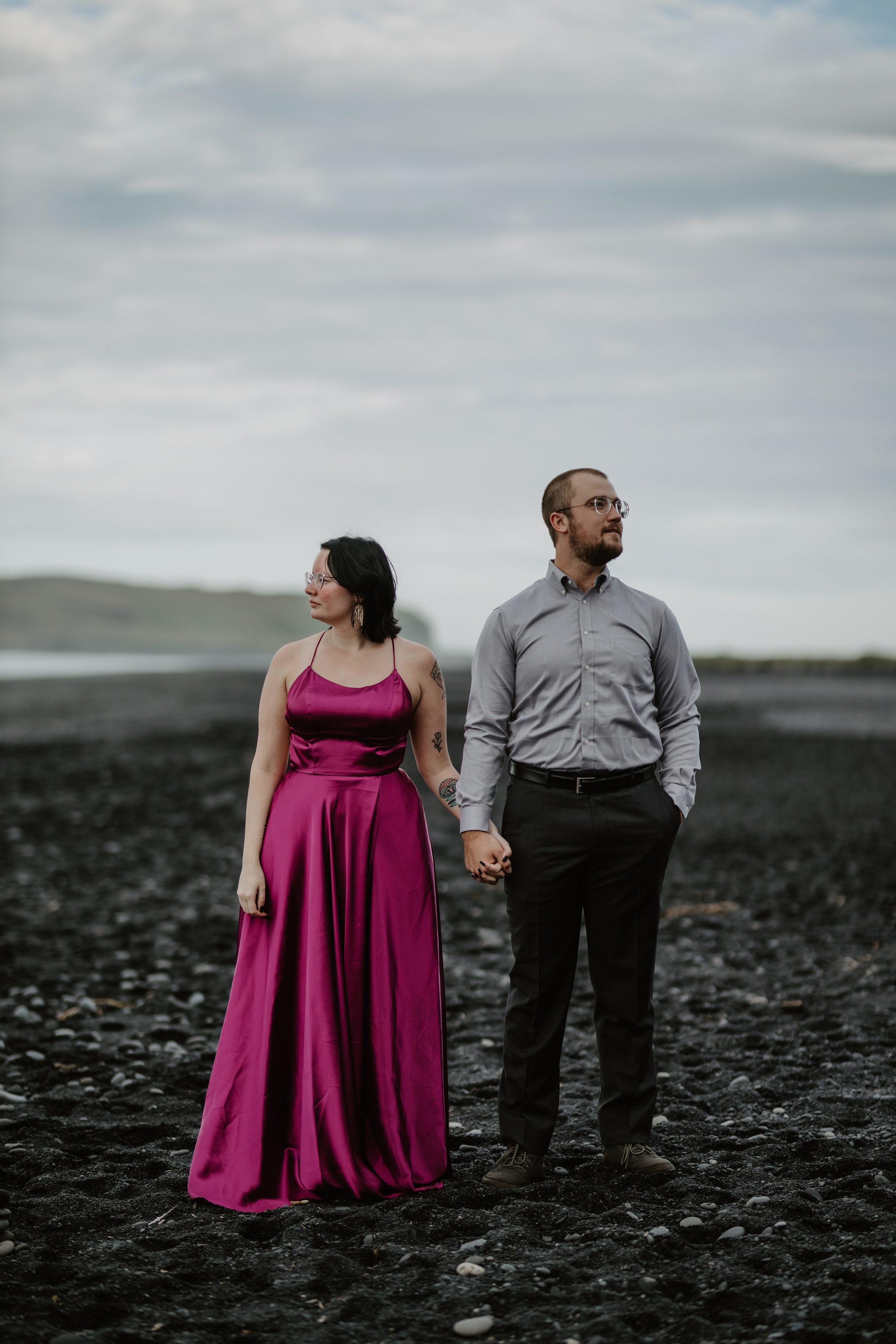 Love and adventure—couple walking along Reynisfjara Beach, Iceland, with the Reynisdrangar sea stacks in the distance.