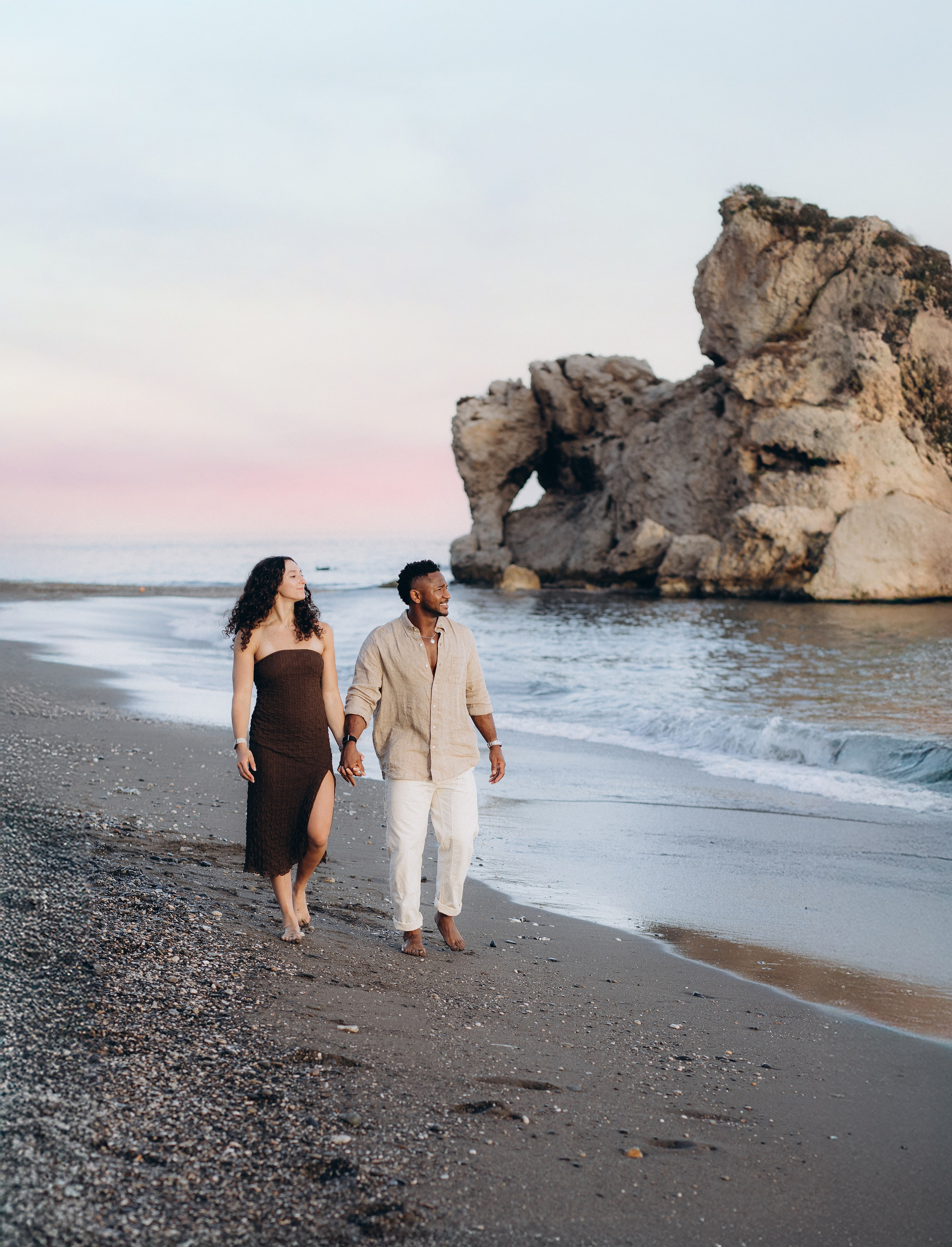 Couple walking hand in hand along a Málaga beach after a sunset proposal. Destination engagement photoshoot on the Costa del Sol capturing relaxed, romantic seaside moments.