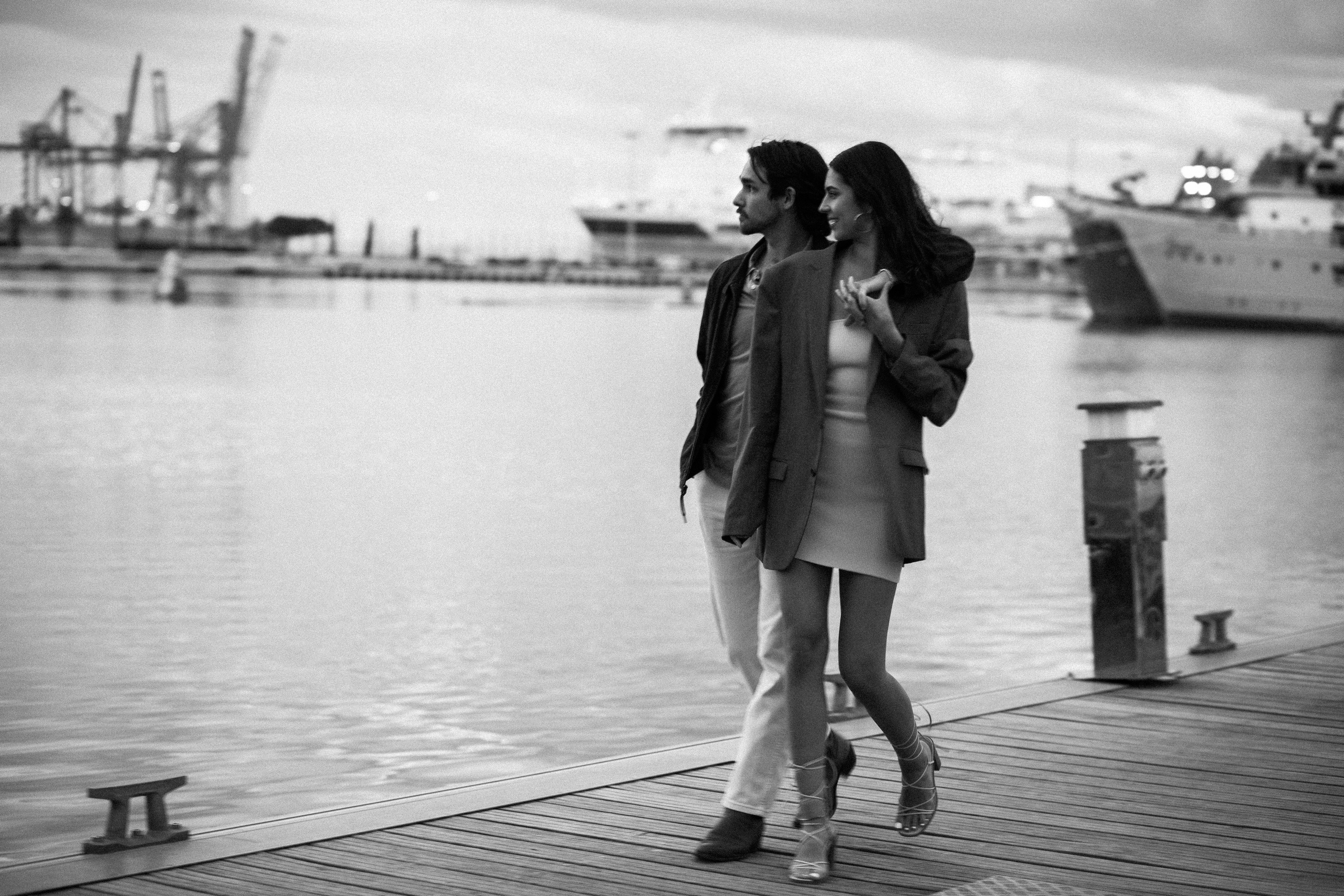 Romantic black-and-white love story photo of a couple walking hand in hand along the marina in Valencia, Spain — ideal for those searching for candid and stylish couple photoshoots in Valencia and across Spain.