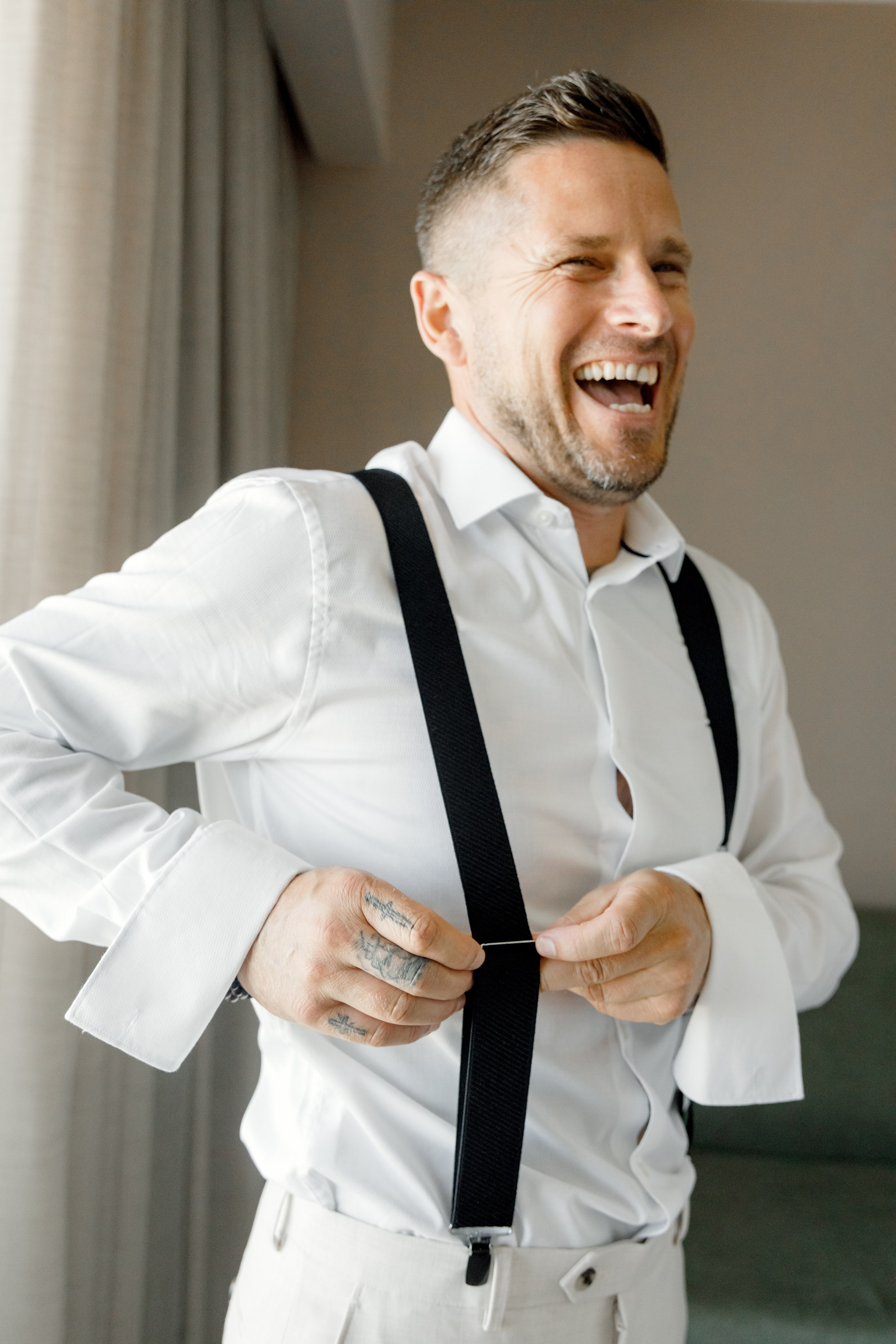 A close-up portrait of the groom's laughing friend, his eyes crinkled with joy and teeth gleaming in a wide, infectious smile. 