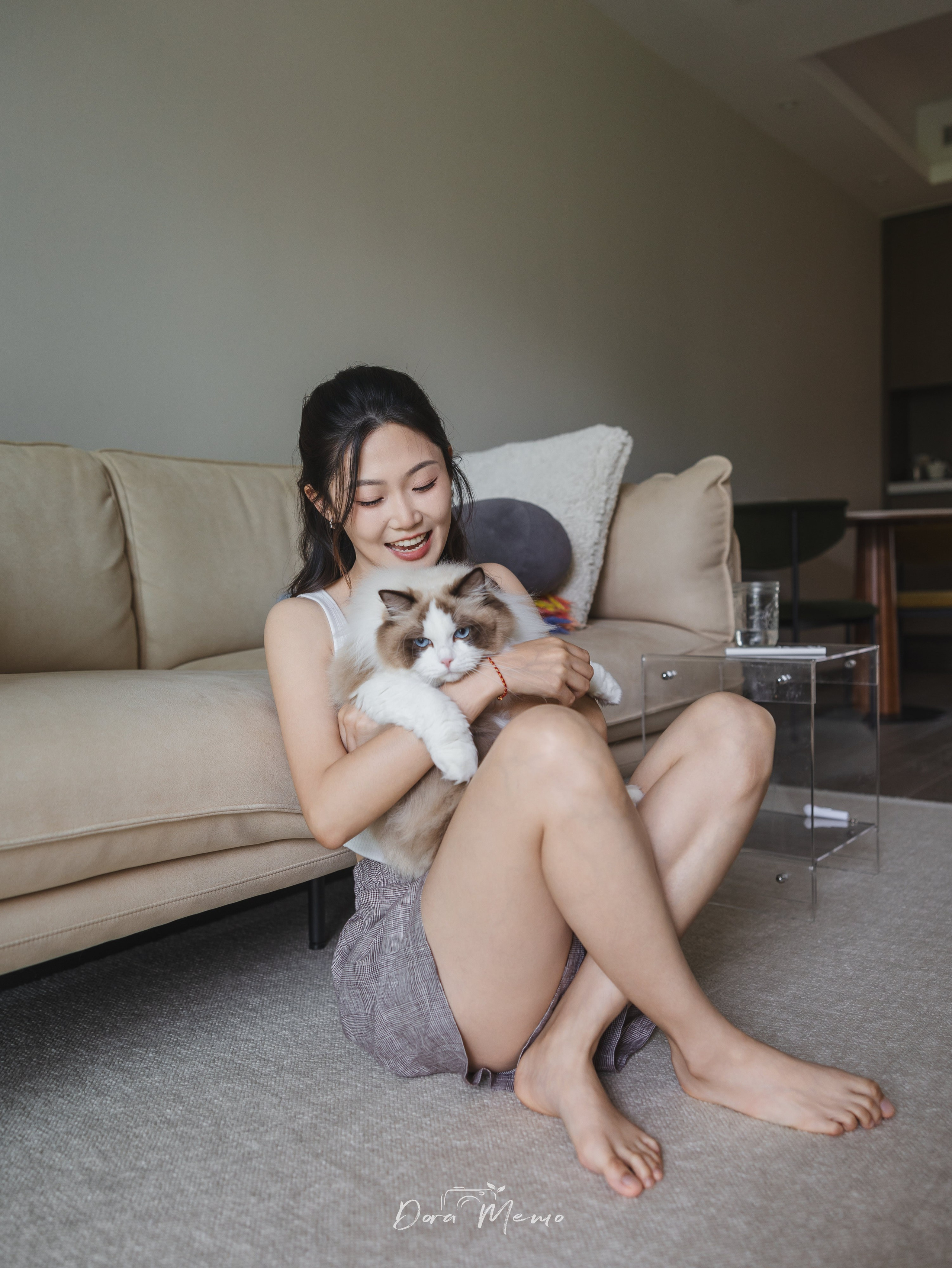 A young woman sits on the floor with her ragdoll cat nestled in her arms, both relaxed in a minimalist living room — a Shanghai family photography moment.