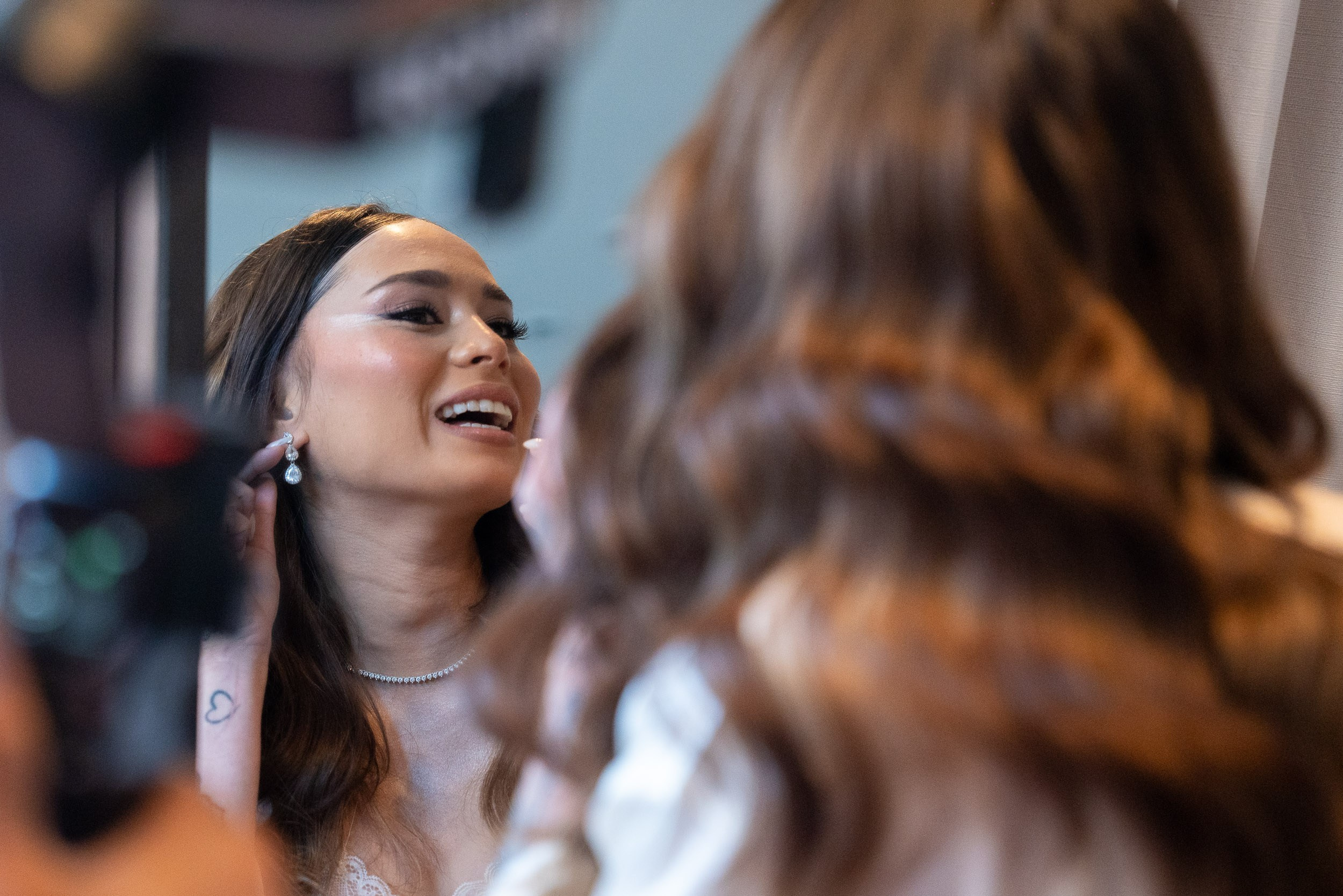 A bride smiles at her reflection as she adjusts an earring