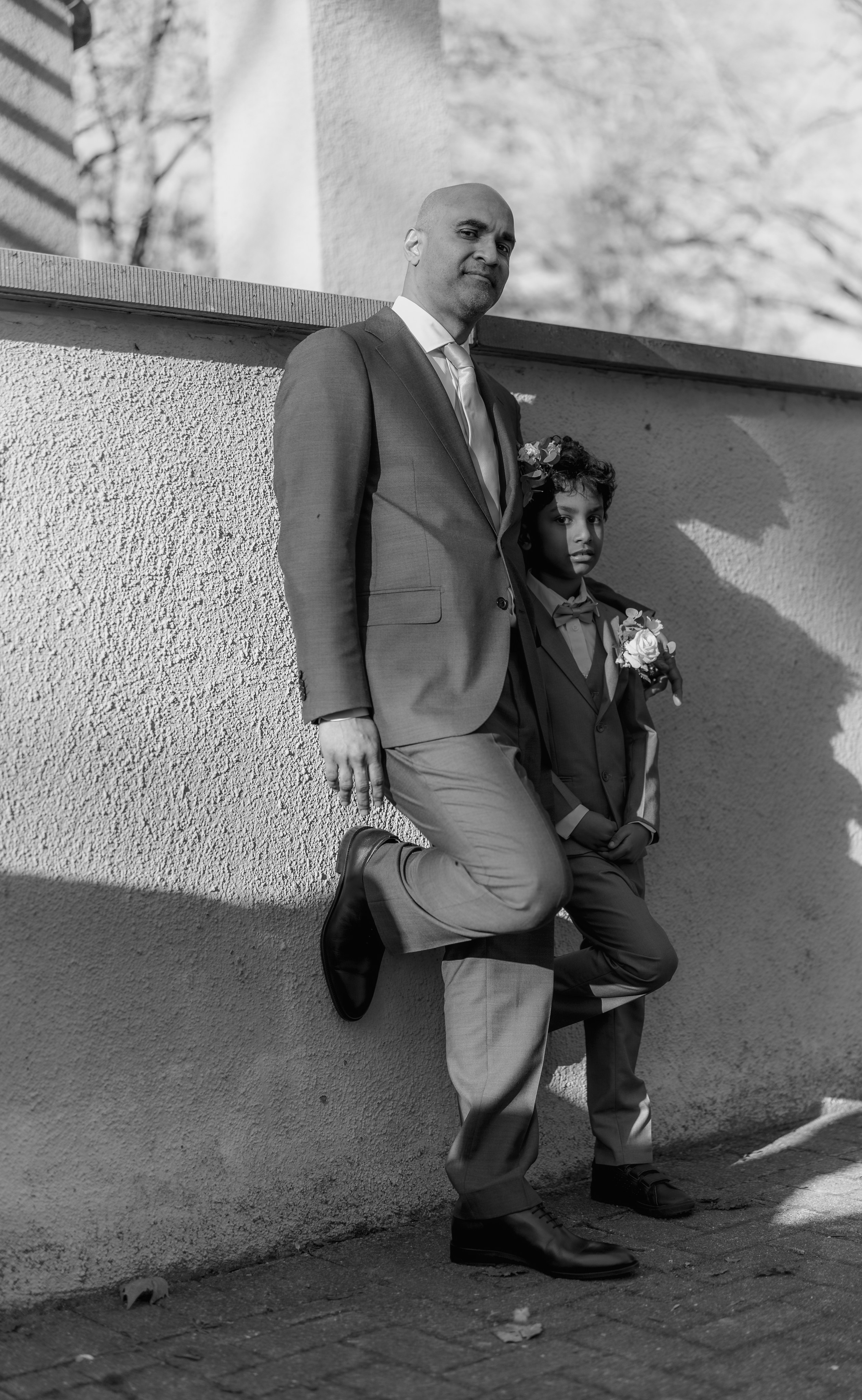 Kapture Fotografie - Artistieke zwart-wit foto van vader en zoon in stoere pose tegen muur met sterke schaduwen