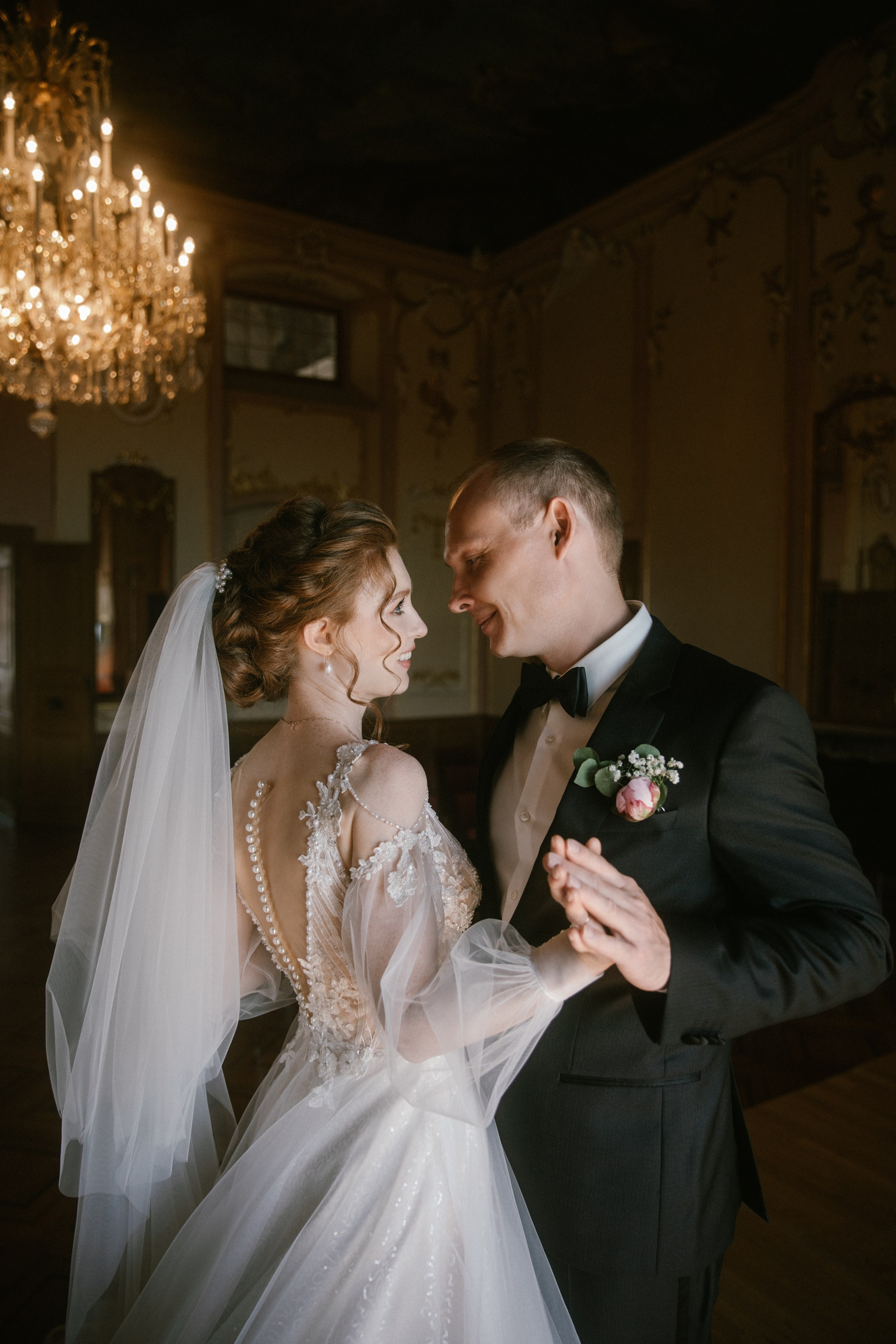 Brautpaar tanzt unter Kronleuchter in Schloss Meersburg, lächelt sich liebevoll an