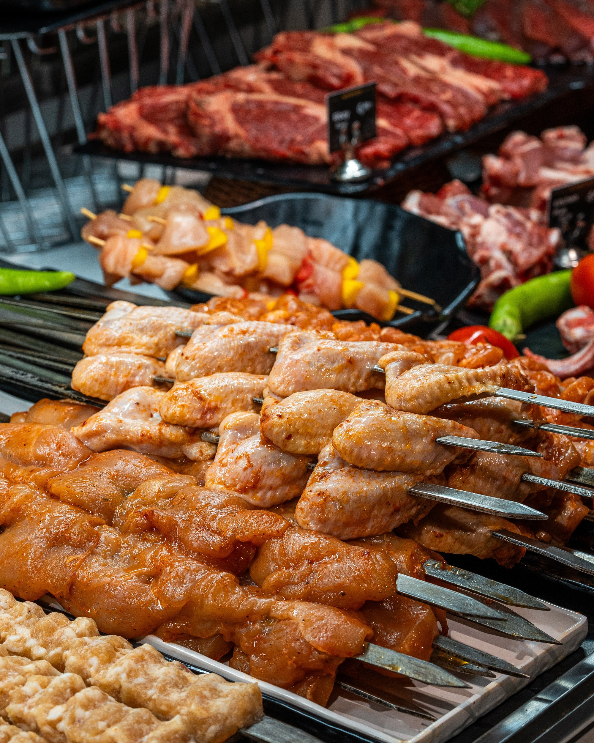 Vitrində sıraya düzülmüş marine edilmiş toyuq qanadları və taxta şişlərdə toyuğun döş əti kababı (şiş kabab), arxa planda digər ət kəsimləri.
