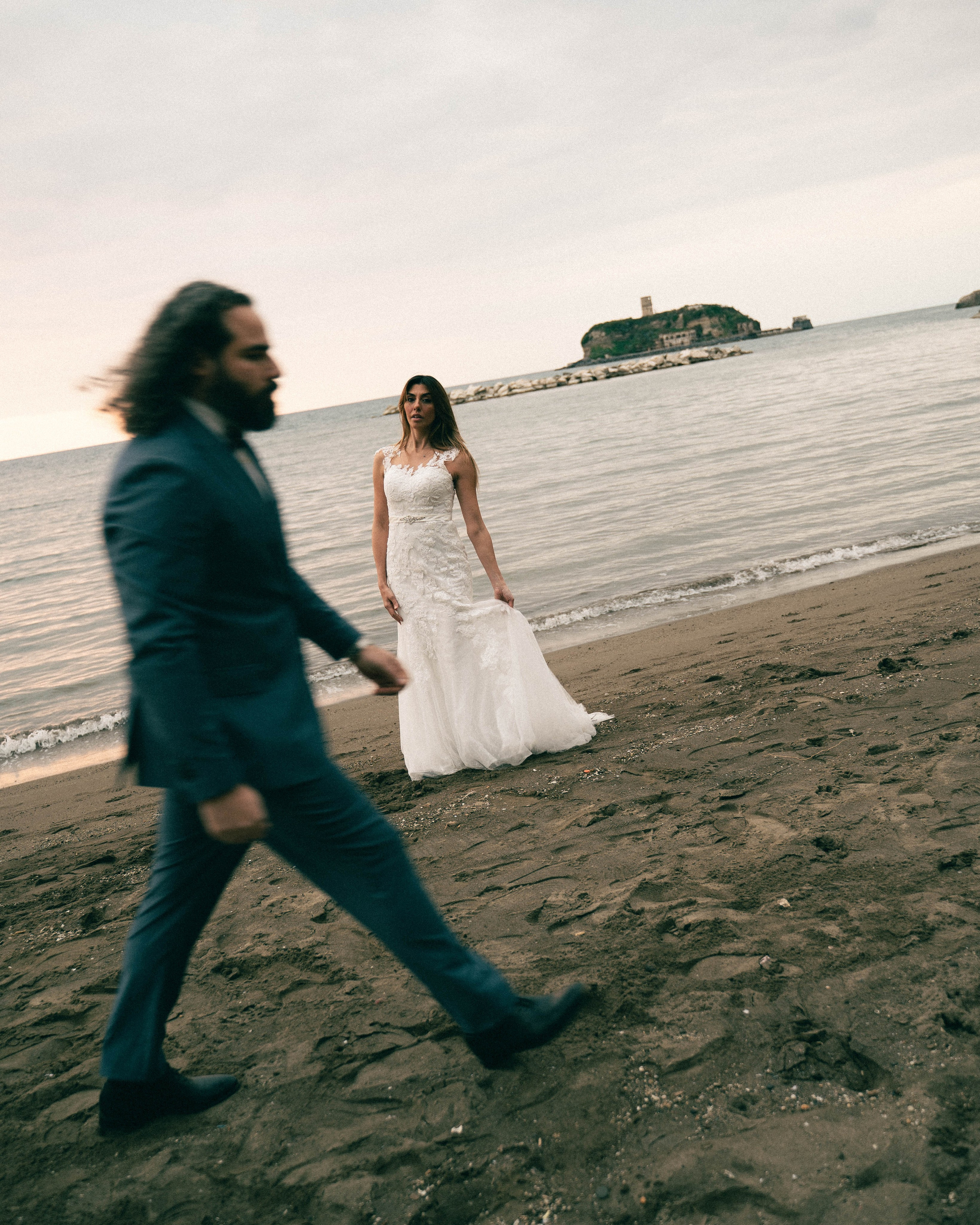 Bride on the shoreline and groom walking in front, beach wedding with motion blur effect