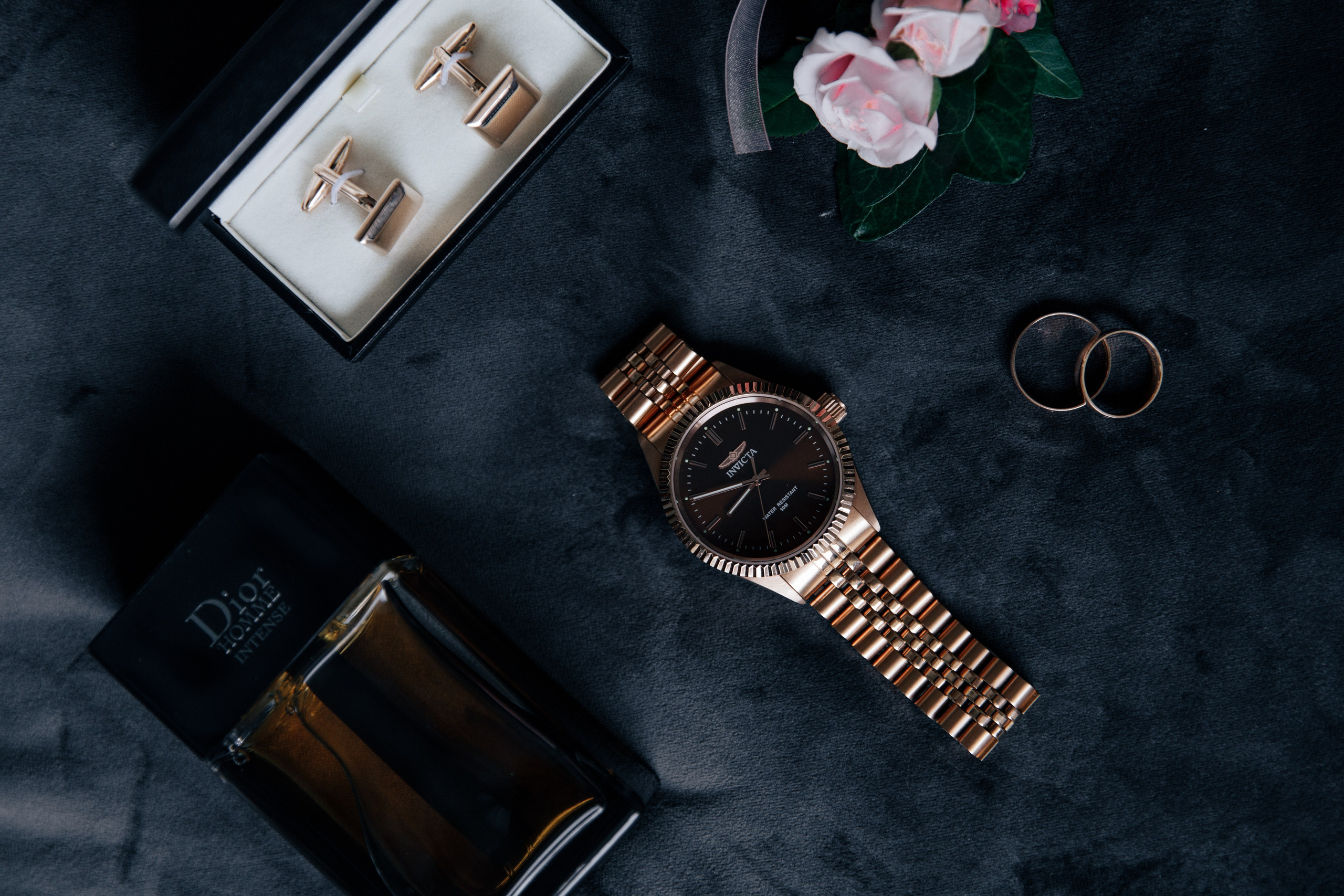 Detailaufnahme des Hochzeitsoutfits des Bräutigams: Uhr, Boutonnière, Parfüm und Manschettenknöpfe.