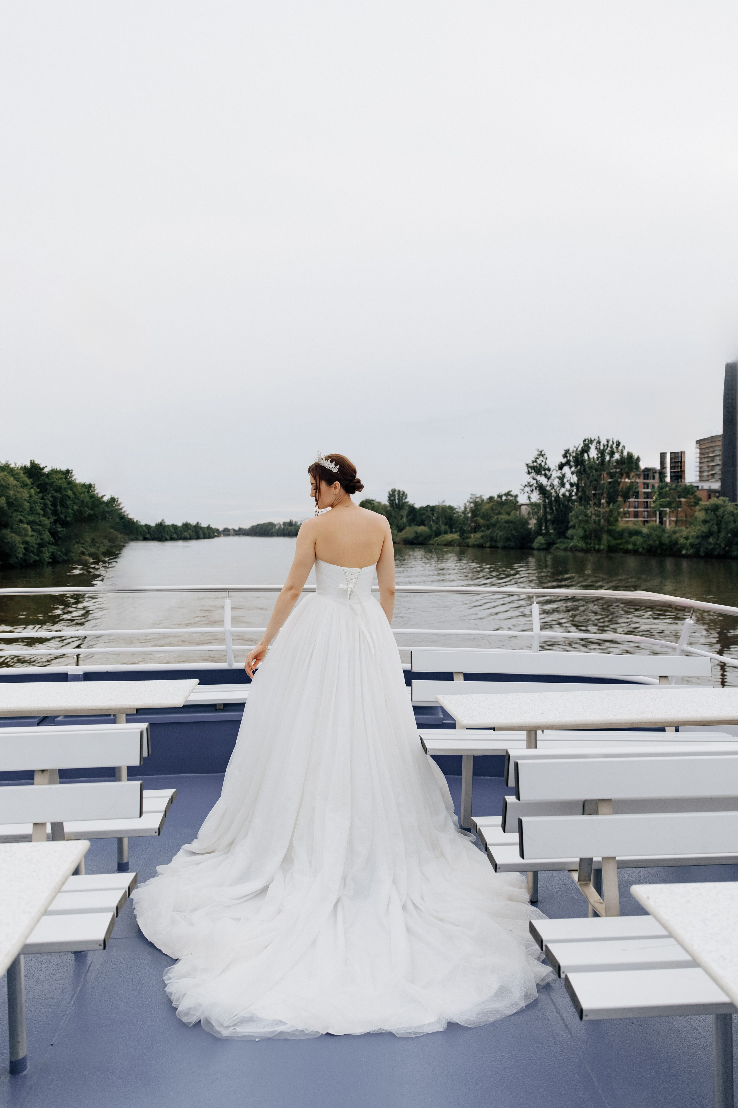 Die Braut geht mit dem Rücken zur Kamera über das Deck, ihr elegantes weißes Brautkleid mit Schleppe weht hinter ihr.