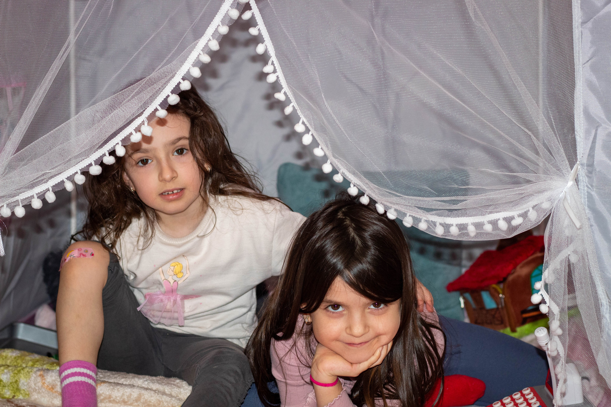 Two children playing inside a homemade indoor tent with cozy fabric drapes.