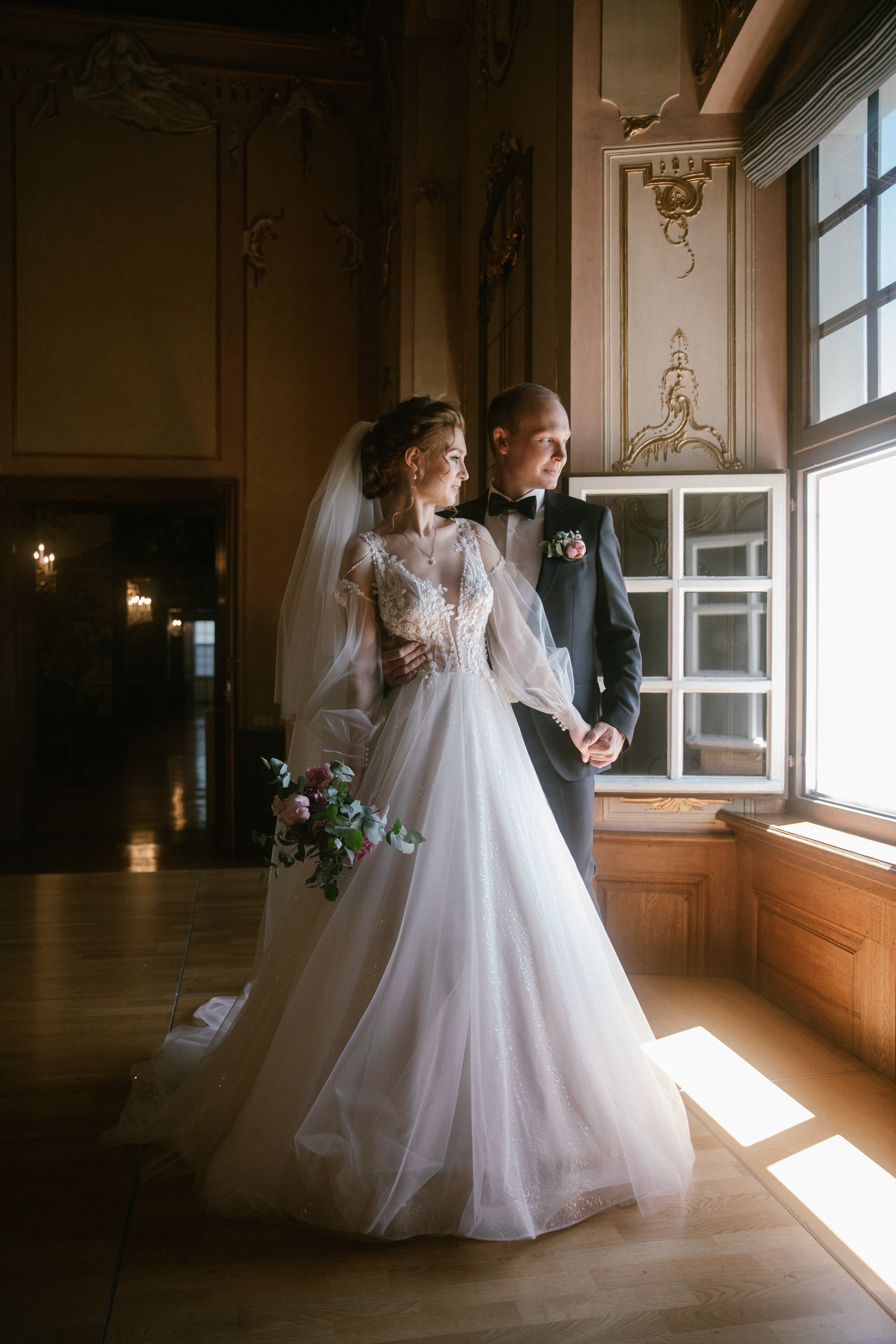 Sonnenlicht fällt auf Brautpaar am Fenster von Schloss Meersburg – Spitze & Blumenstrauß