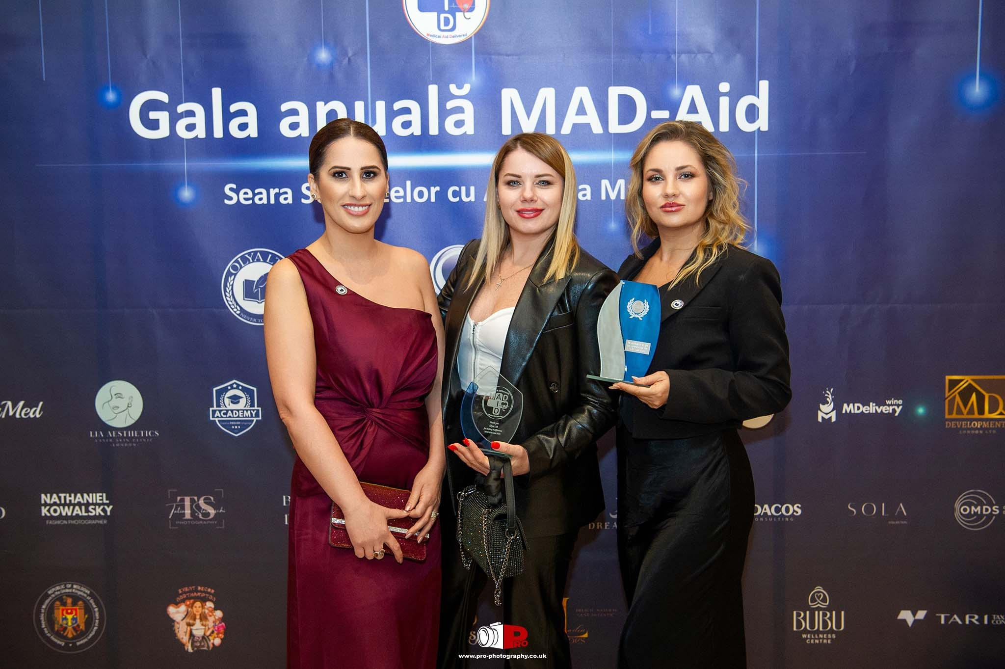 Three women holding awards at the MAD-Aid Gala, celebrating achievements and contributions.