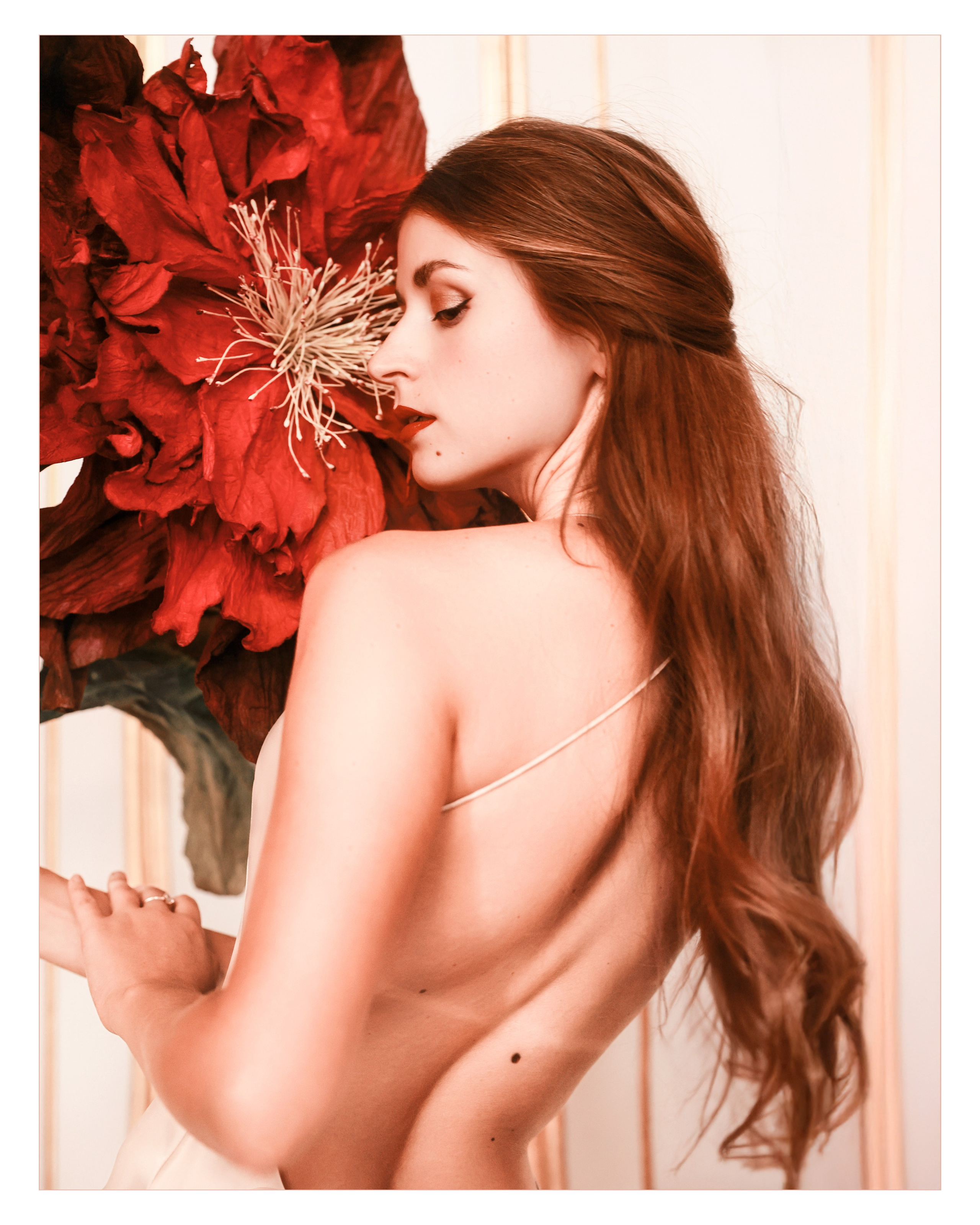 Porträt einer Opernsängerin mit rotem Lippenstift und Perlenohrring vor einer großen roten Blume – stilisierte Fotografie im Schloss Mirabell in Salzburg.