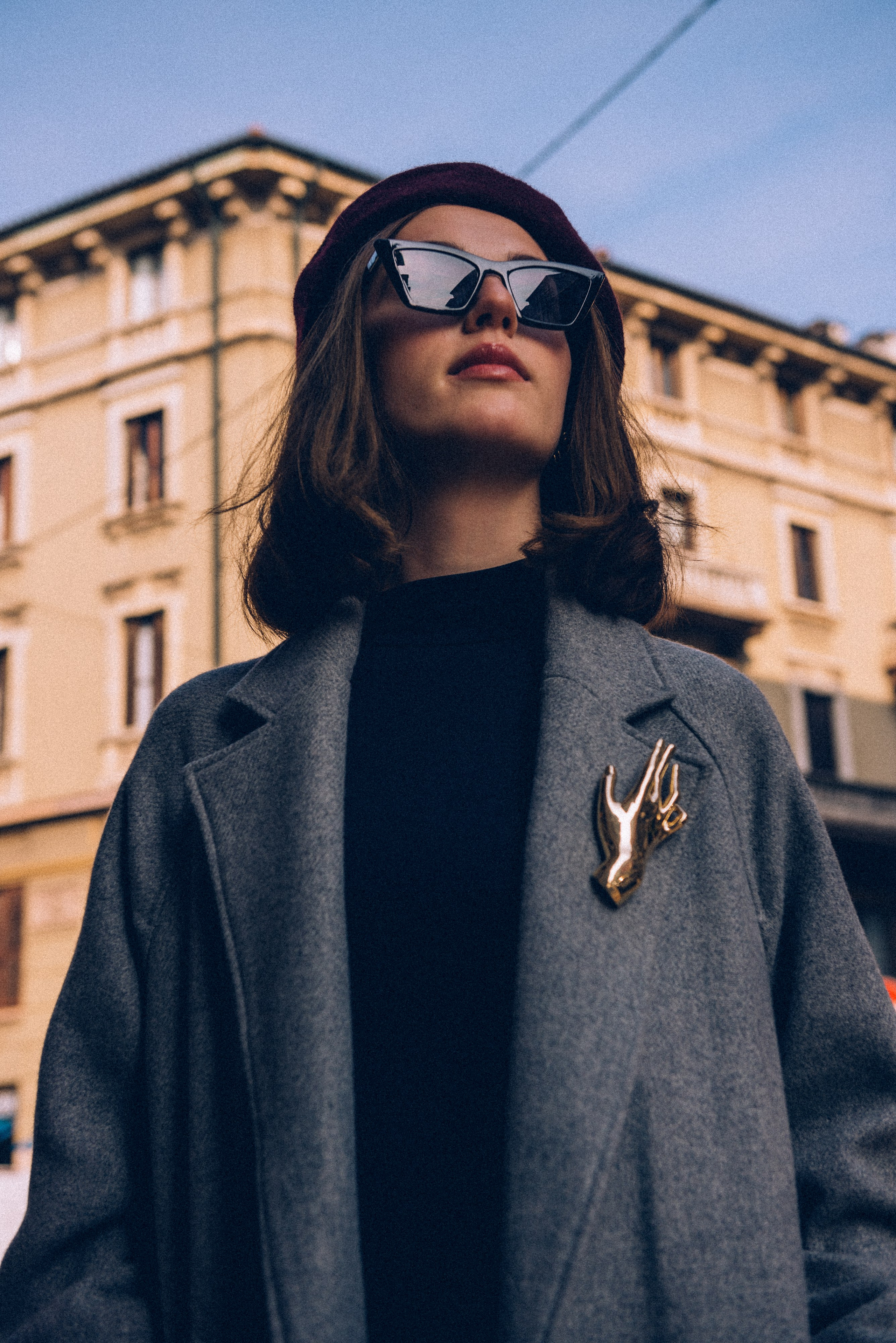 Modern street fashion photography in Milan: a woman in a gray coat poses confidently near iconic Milanese architecture