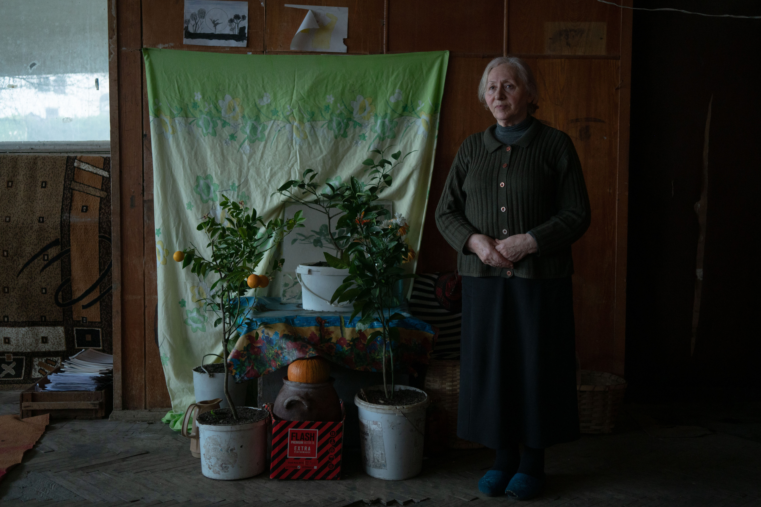 Tsitsino Kvirtia stands near her improvised  lemon garden in the hall of the former club at the Imereti Sanatorium. When Tsitsino was forced to flee the city of Gagra in Abkhazia, she was 40 years old. She had a two-storey large house by the sea, in which they lived with her extended family. When her brother was captured, they were offered a ransom. They gave everything they had in their house. When the brother came back they immediately fled with the whole family. They were put in one room of the sanatorium. Tsitsino’s husband died, the children left. She lives alone. She still hears the smell of the sea everywhere, which she misses so much.