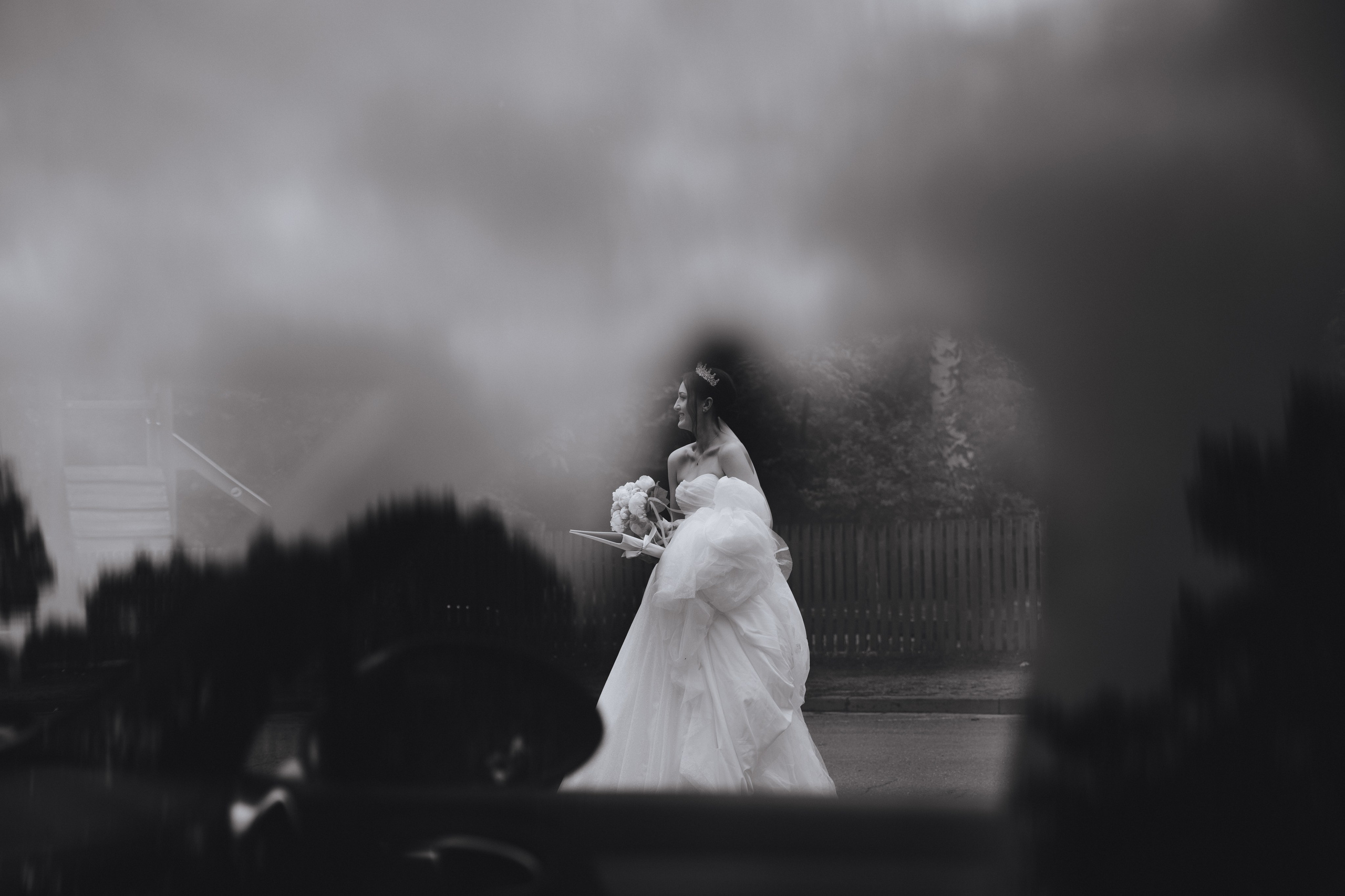 Schwarz-Weiß-Foto der Braut, aufgenommen durch das Glas des Autos.